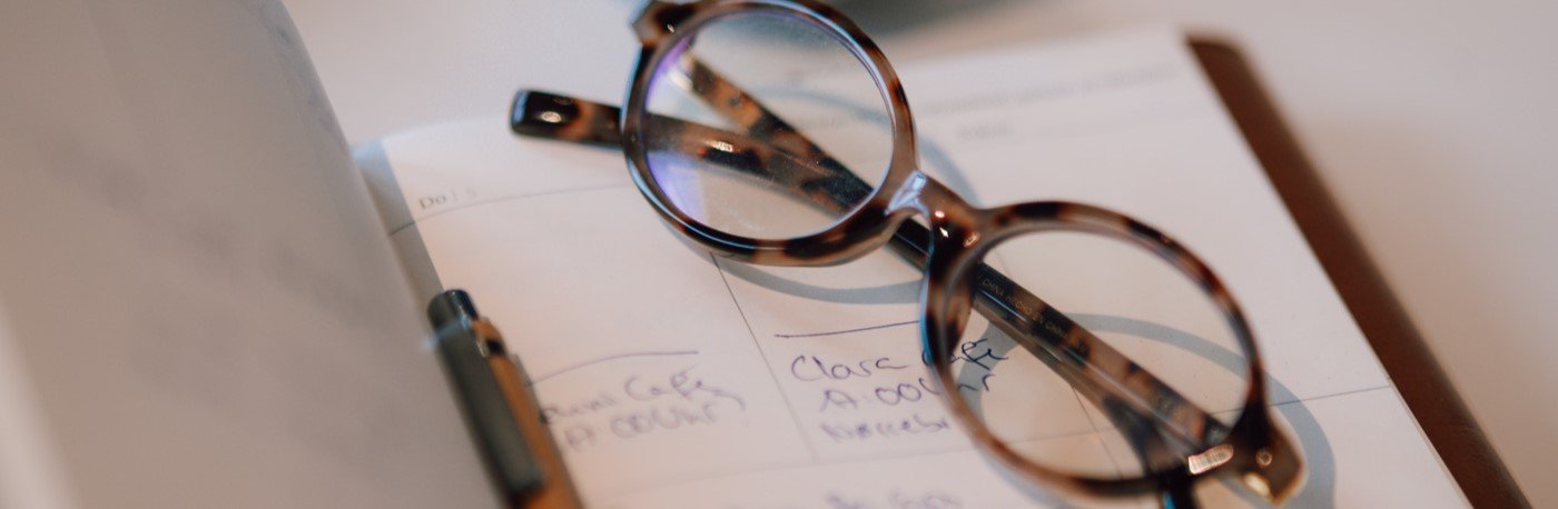 A pair of tortoiseshell eyeglasses resting on an open planner or notebook with handwritten notes.
