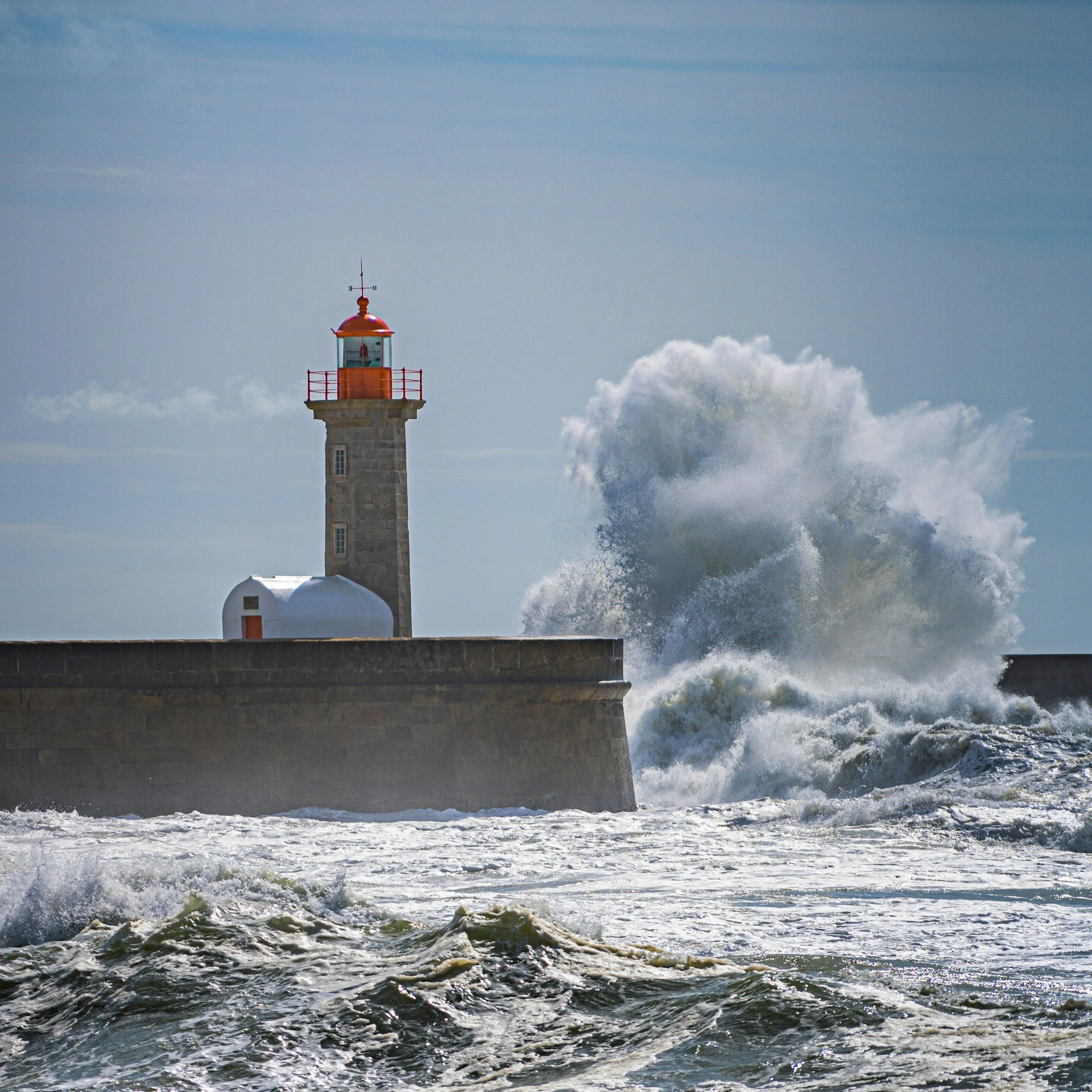 Leuchtturm am Meer bei stürmischer See mit hohen Wellen, die gegen die Mole schlagen.