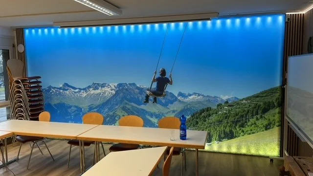 Große Wanddekoration mit Mountainbike-Fahrer im Hintergrund, das im Sinne einer 3D-Tapete fotografiert wurde, vor einer Berglandschaft mit blauen Himmel.