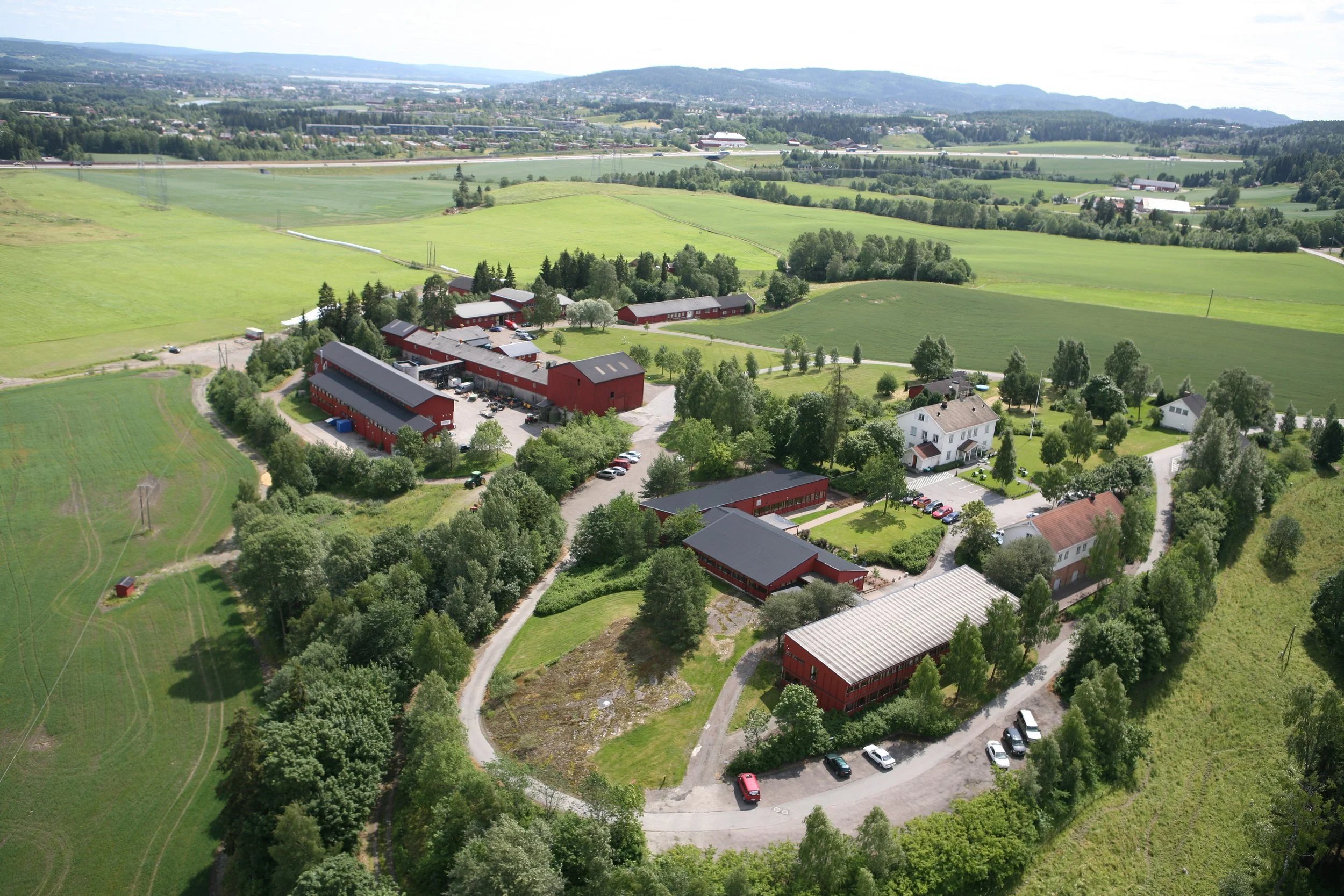 Landskap av grønne åkre, skoger, bygninger og veier sett fra luften.