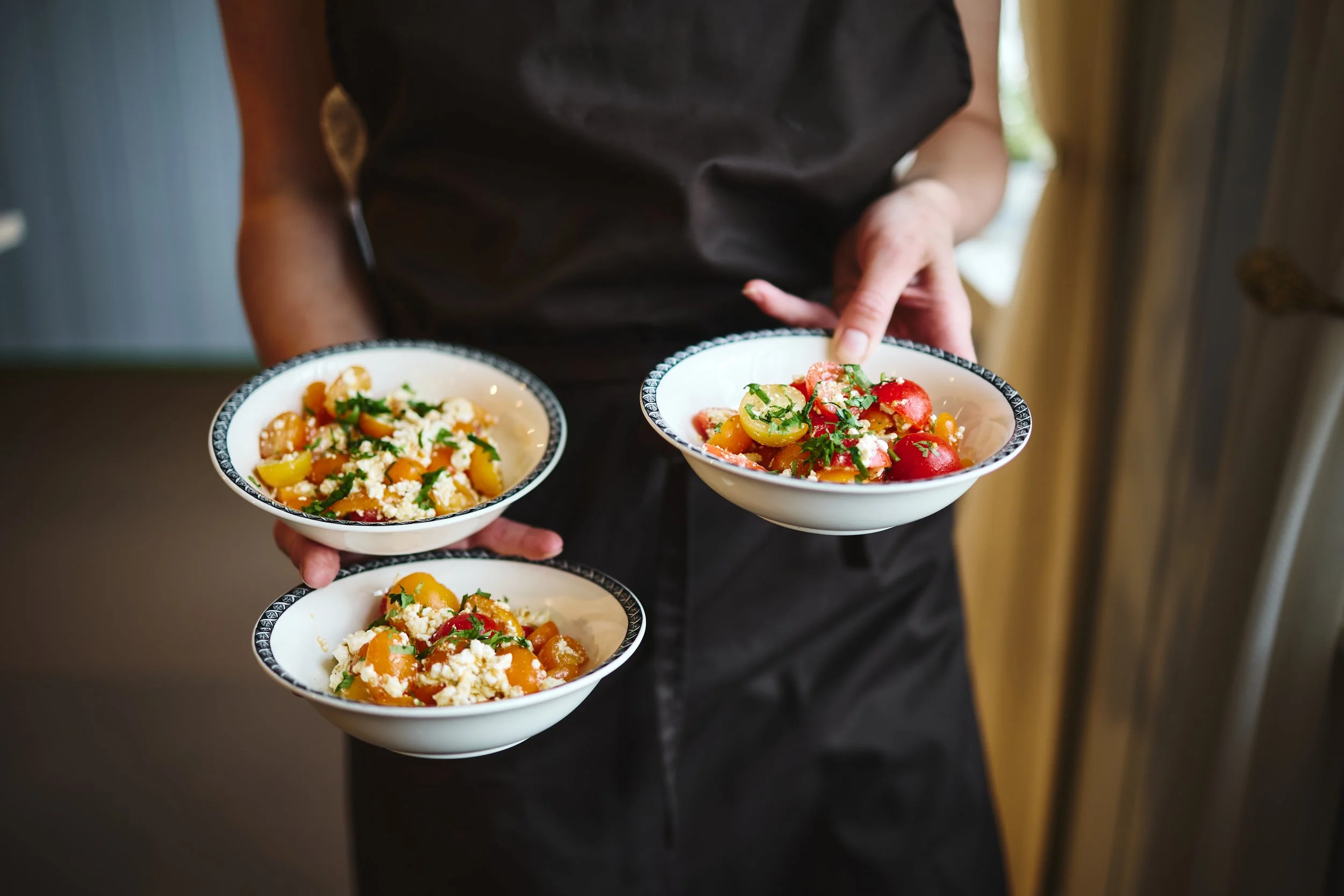 Person som bærer tre skåler med salat med tomater, paprika, og urter.