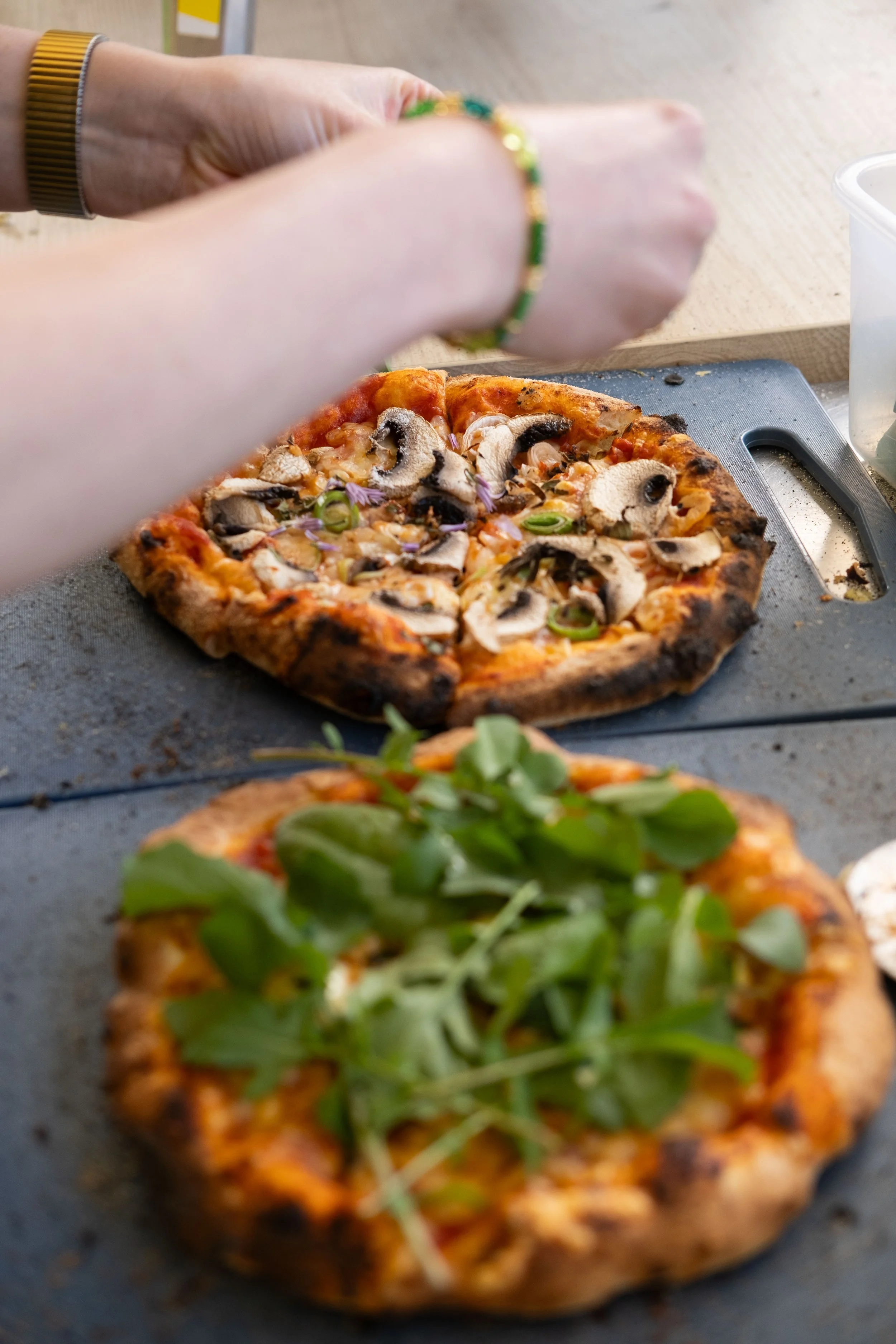 Nærbilde av en pizza med sopp, løk, og grønne urter, plassert på en skjæreflate.