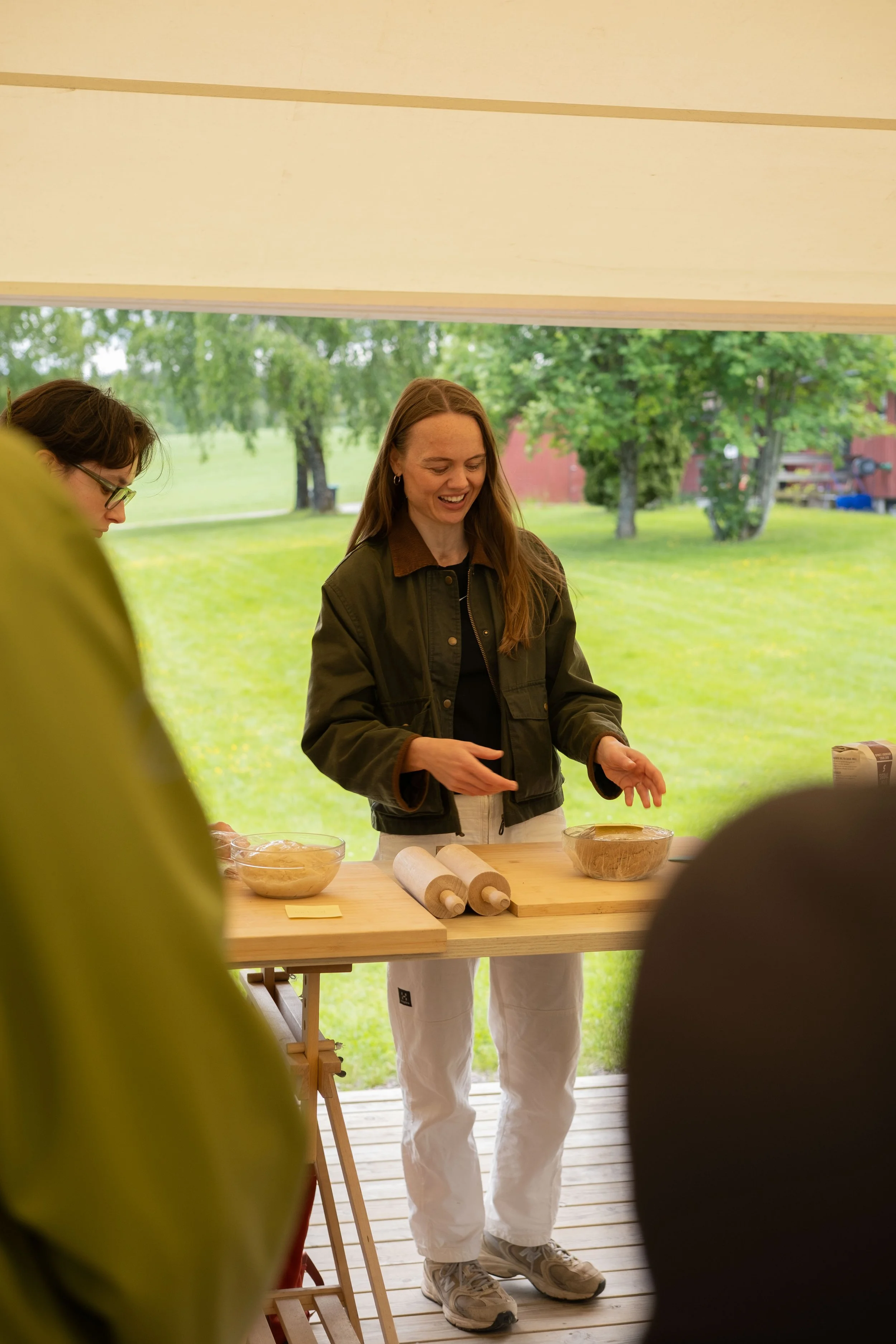Kvinner som deltar i en matlagingsaktivitet under en festival eller utendørsarrangement, med ett bord som har en kjevle og skåler med deig.