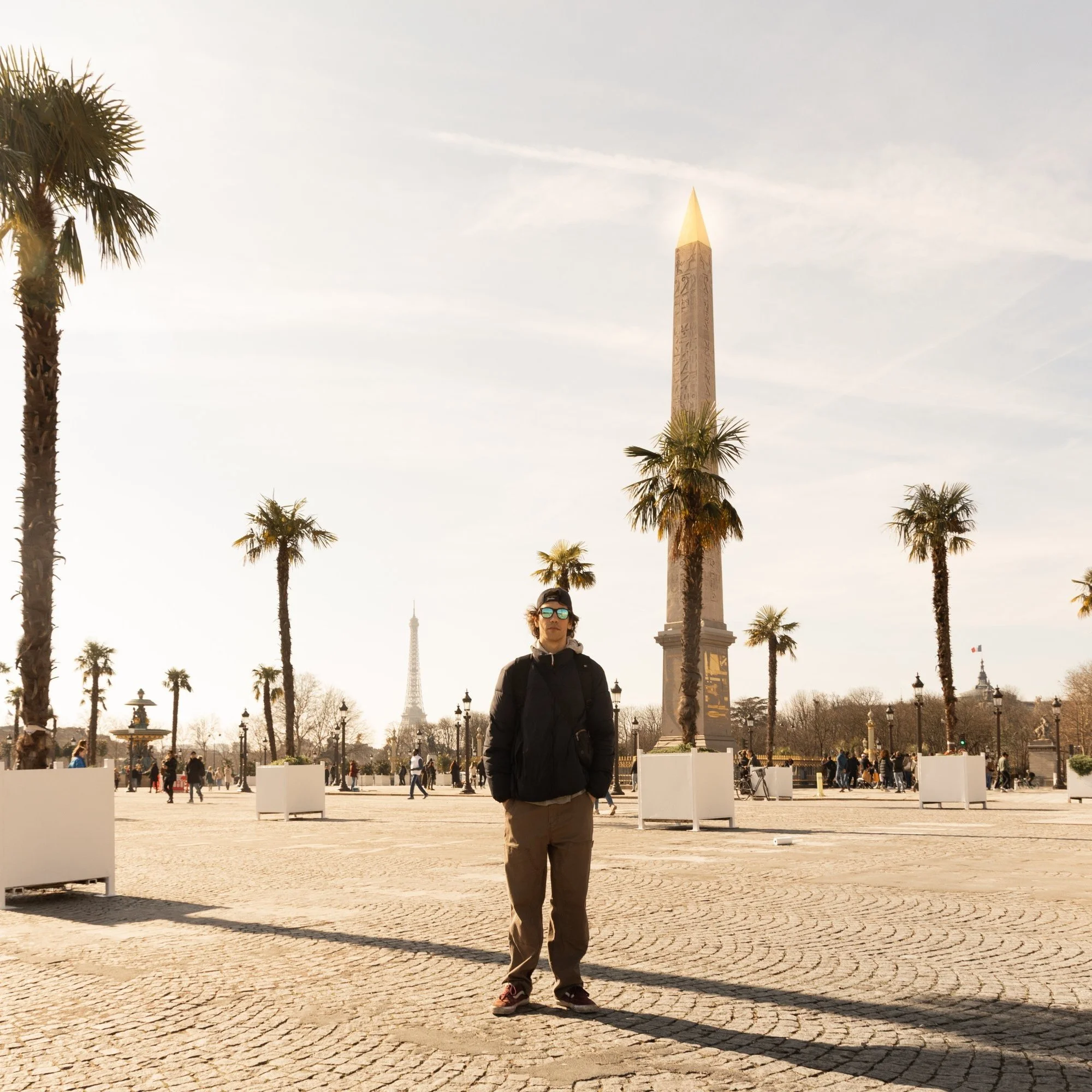A person standing in front of the Luxor Obelisk at Place de la Concorde in Paris, with palm trees and the Eiffel Tower in the background during daytime.