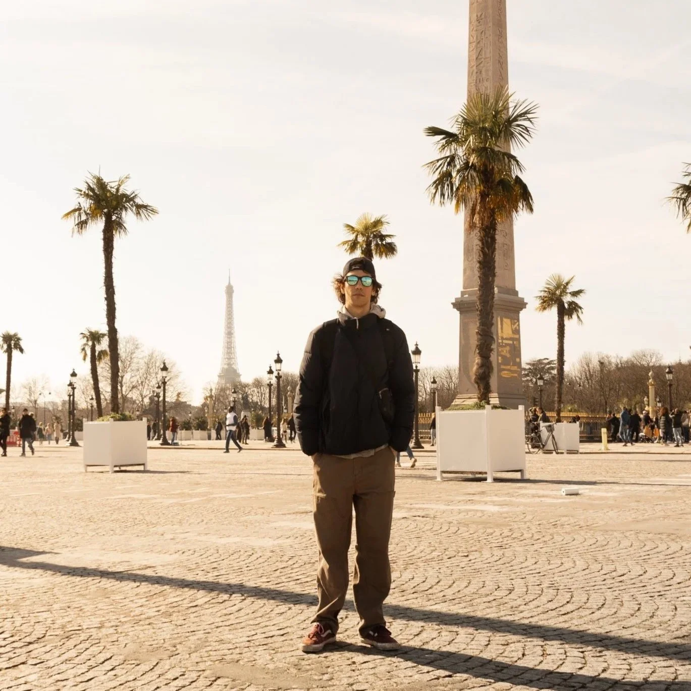 A person standing in front of the Luxor Obelisk at Place de la Concorde in Paris, with palm trees and the Eiffel Tower in the background during daytime.