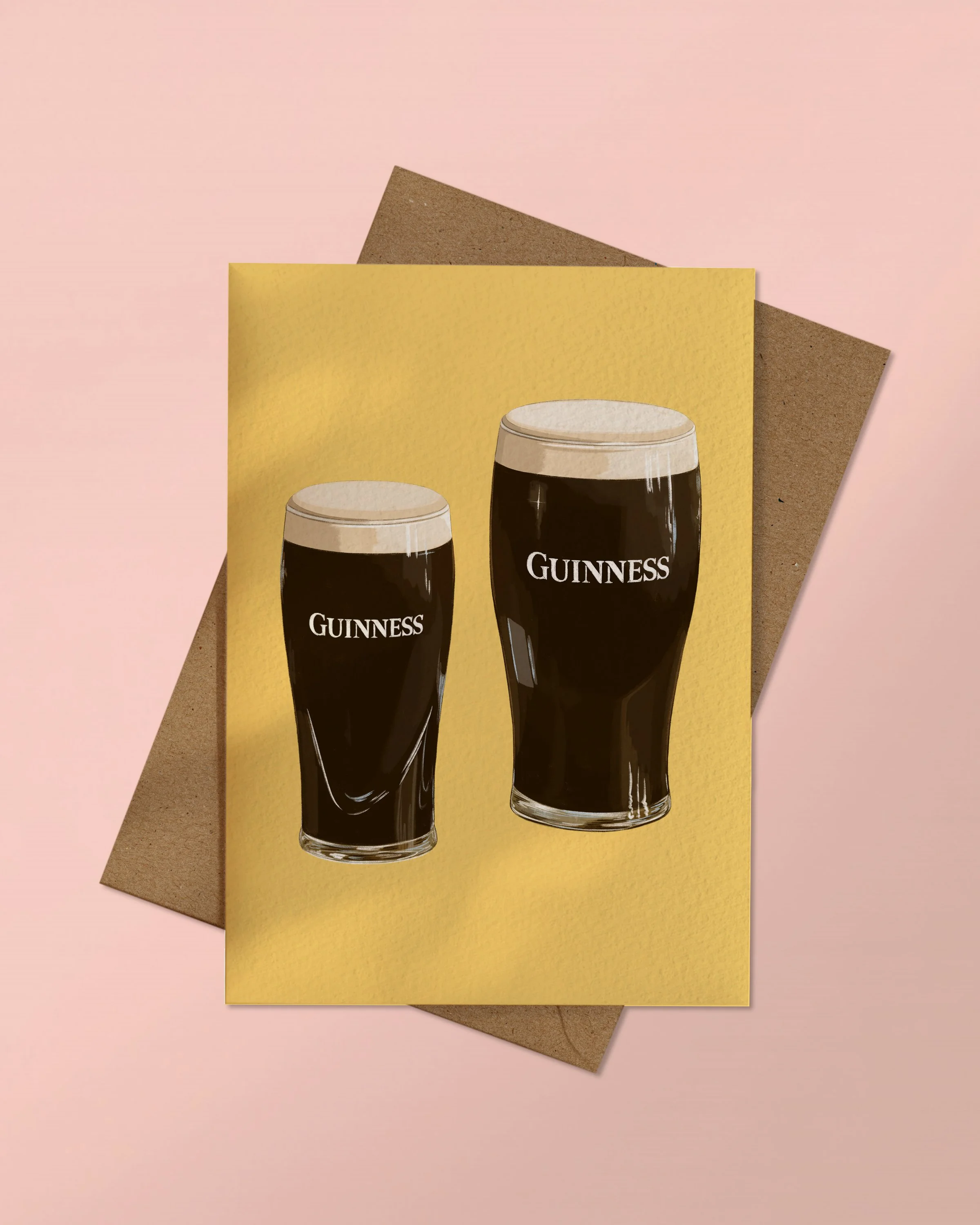 A6 Greeting Card of a pint and a half of Guinness on a yellow background stacked on a kraft brown envelope on a pink background.