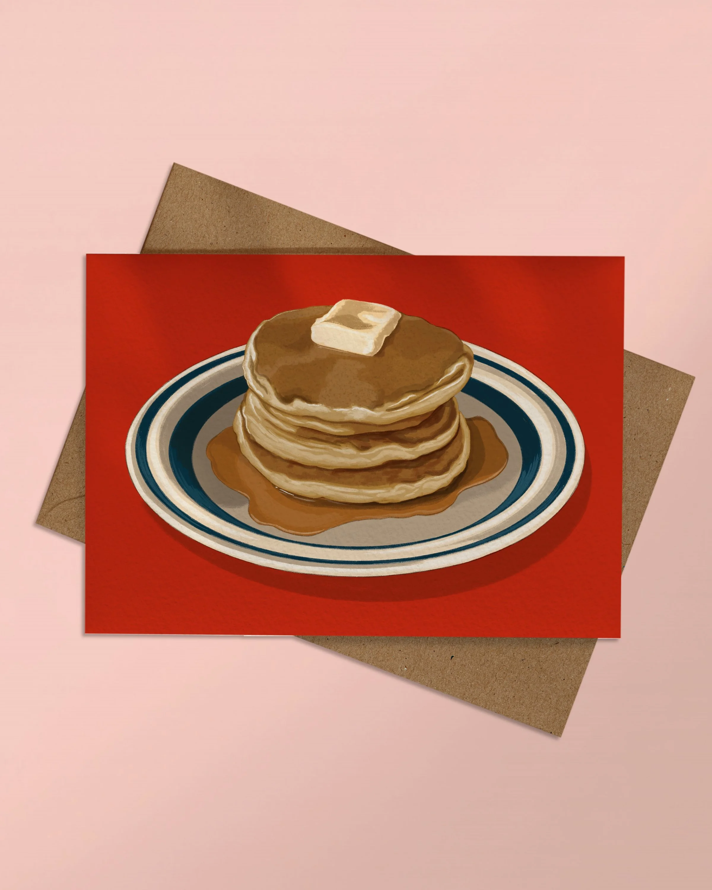 A6 Greeting Card of a plate of pancakes on a red background stacked on a kraft brown envelope on a pink background.