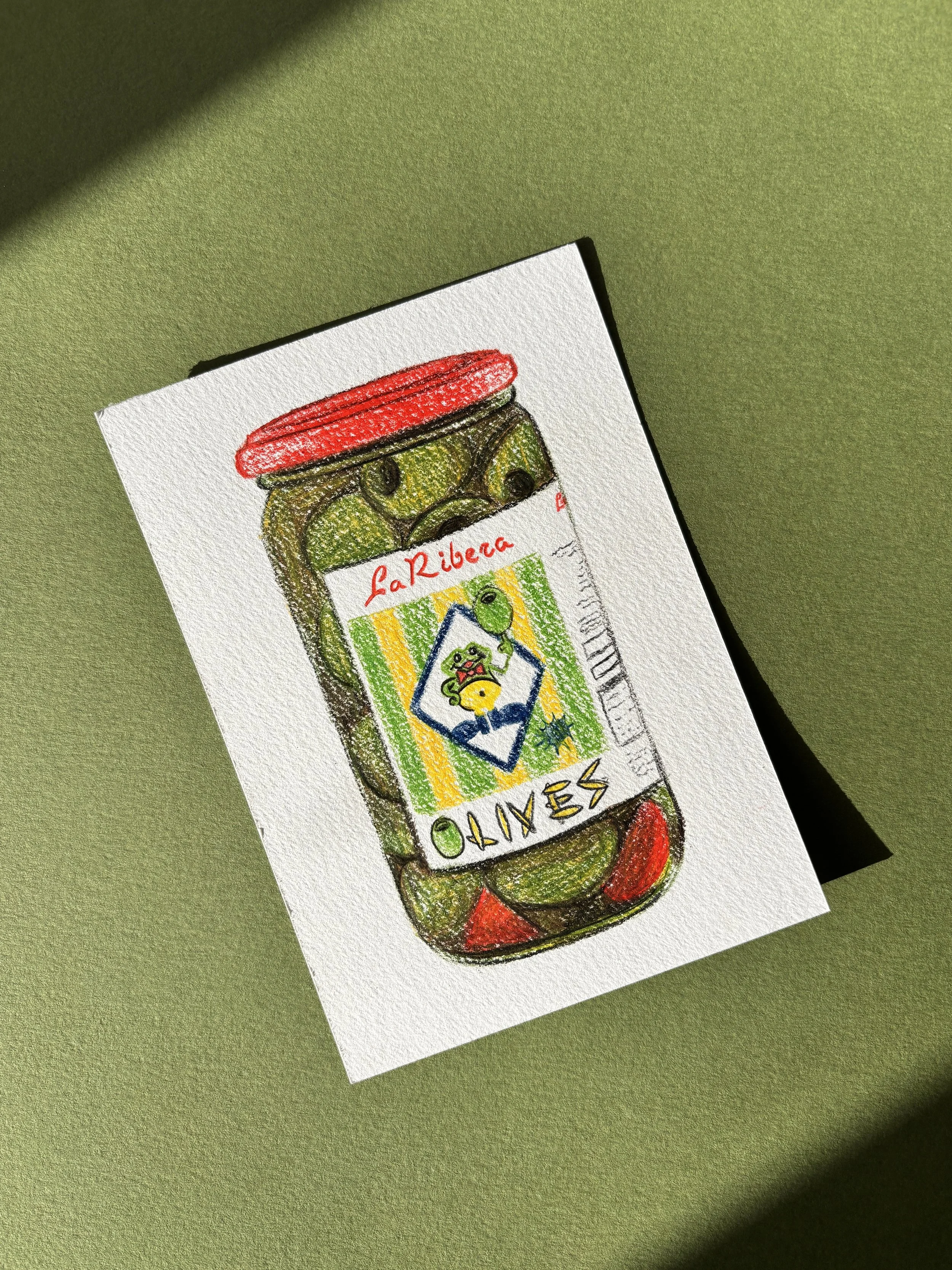 A crayon drawing of a bottle of Olives with a colorful label featuring a cartoon olive and yellow and green stripes, on white paper with textured surface, on a green background.