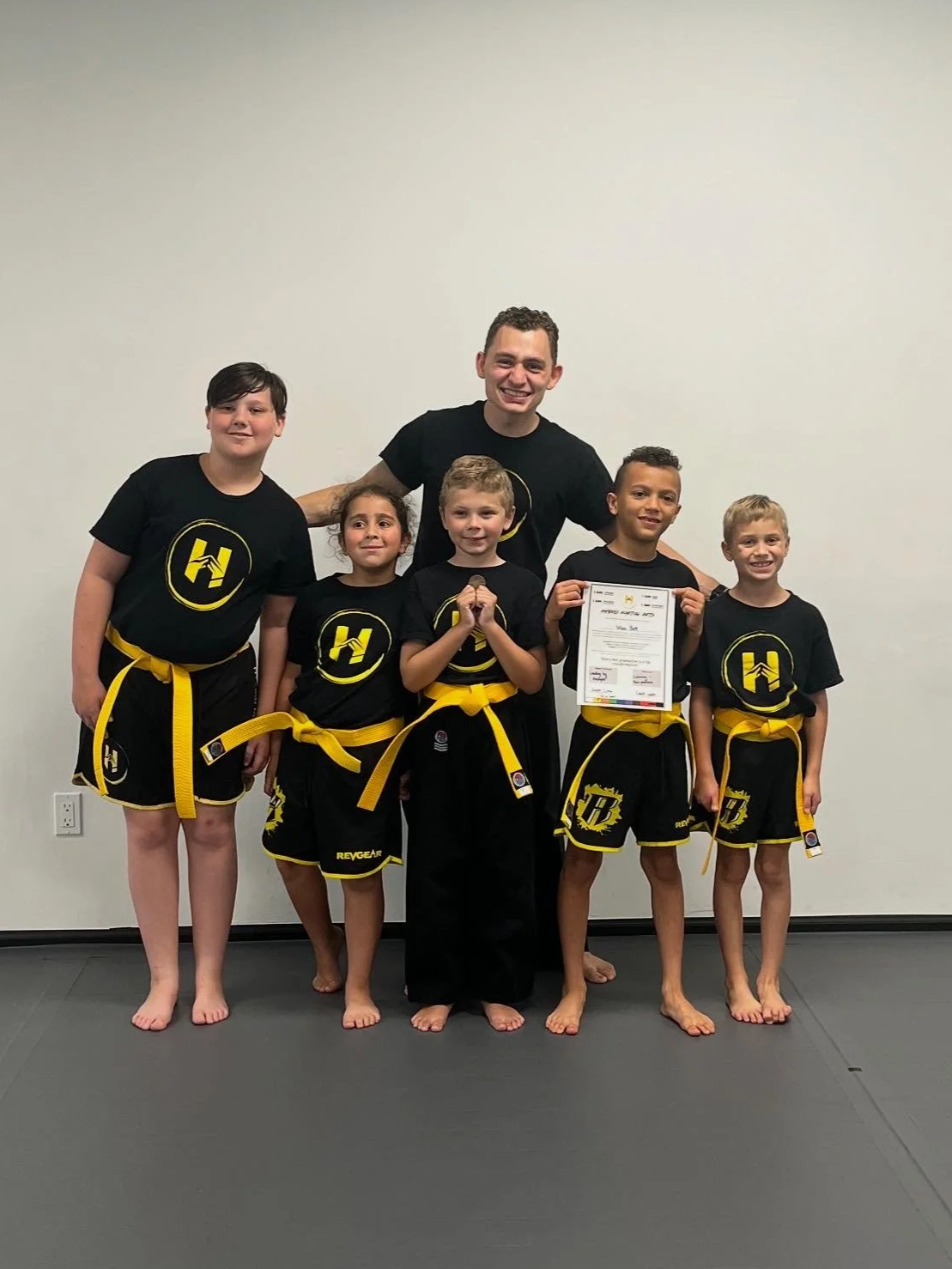 Group of kids in martial arts uniforms with an instructor, holding a certificate.