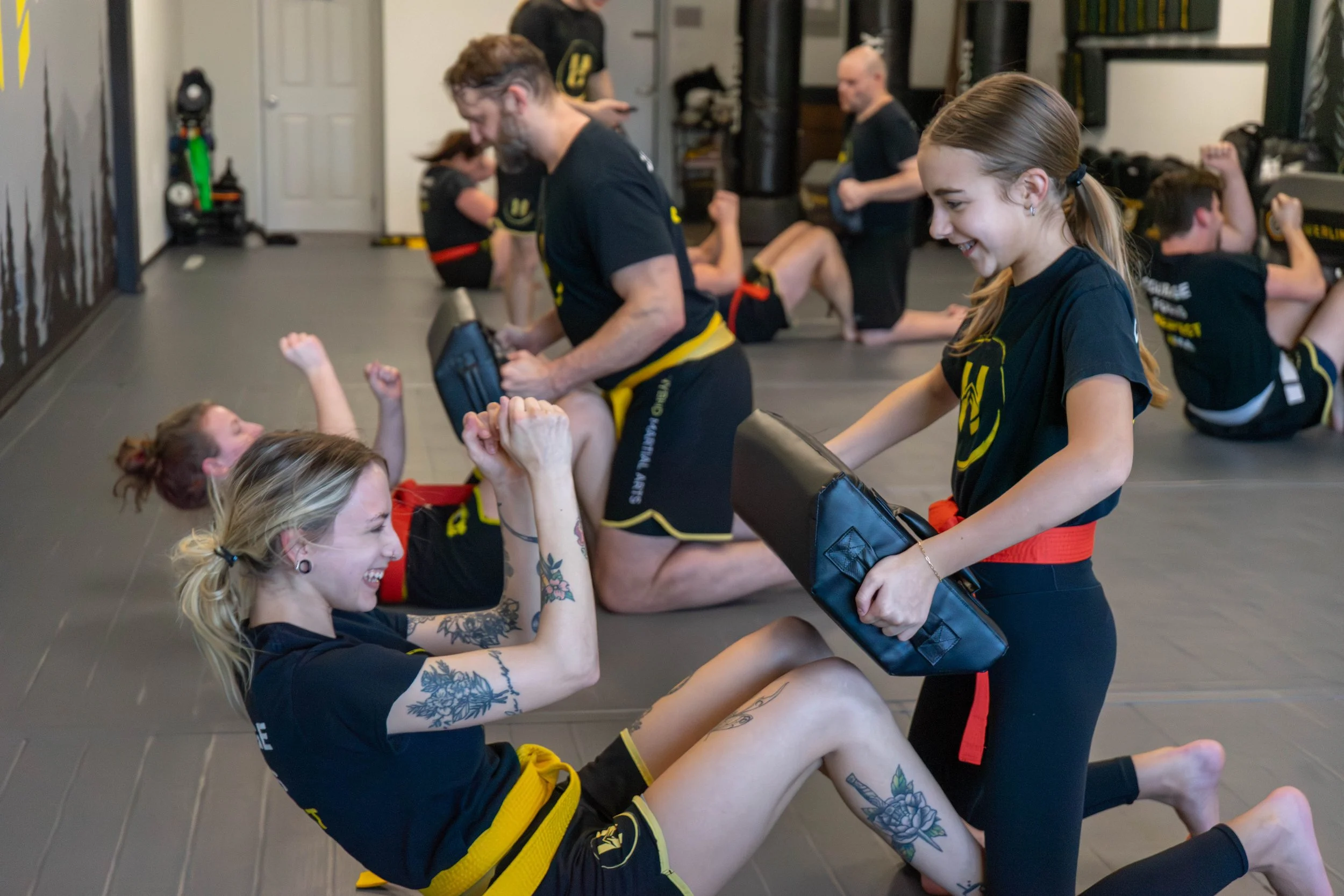 Martial arts class with women practicing submission techniques and smiling while training in a gym.