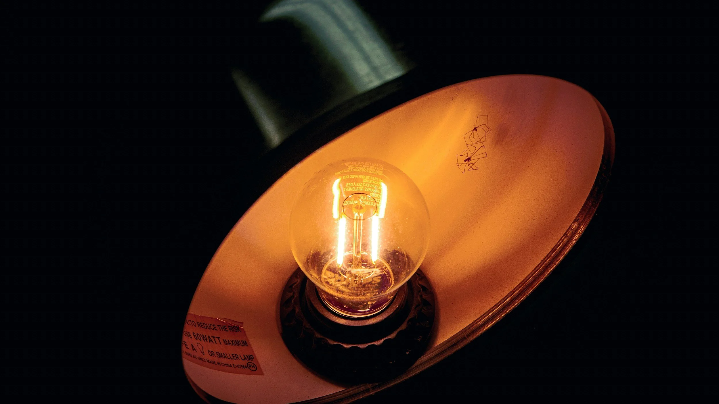 Close-up of a glowing filament inside an illuminated incandescent light bulb, partially enclosed in a copper-colored reflector.