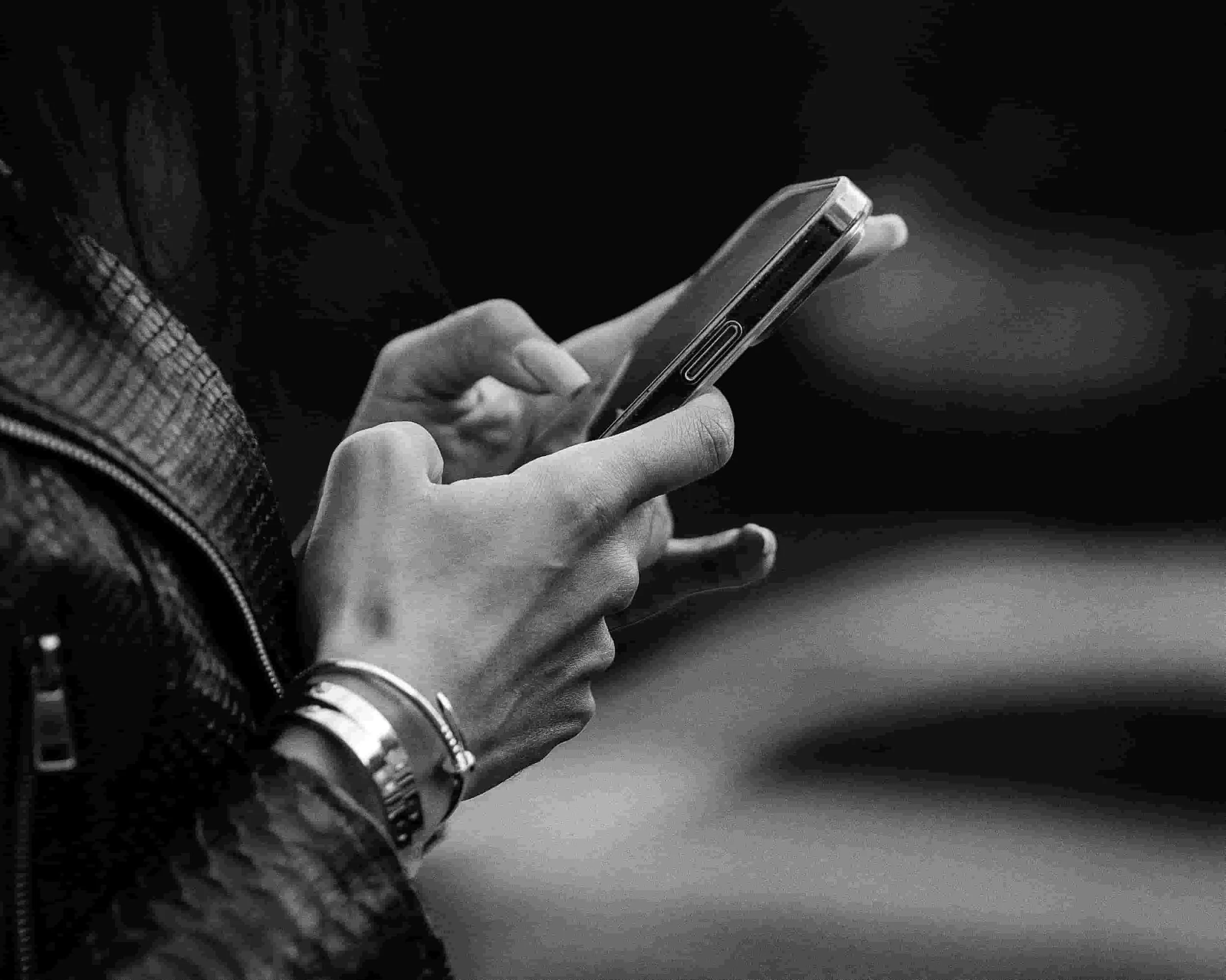 Close-up of a person holding a smartphone, wearing a watch and bracelet, with a dark background.