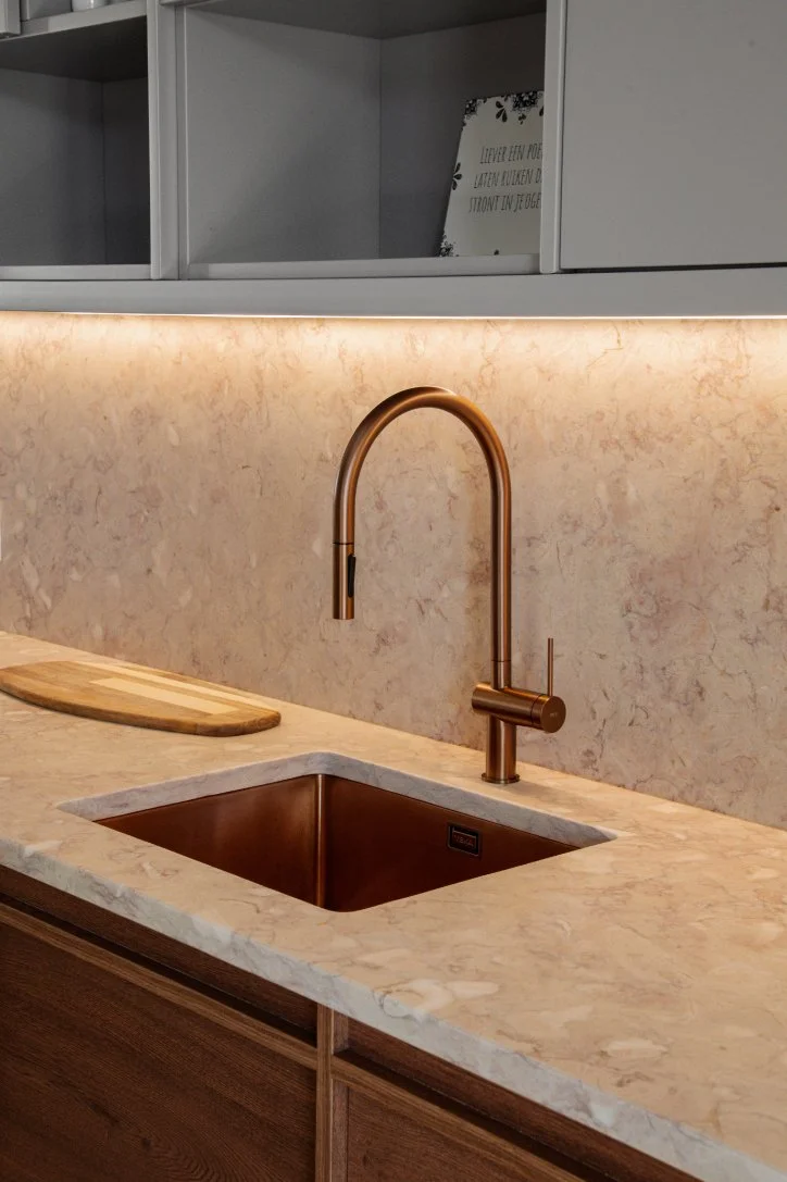 A modern kitchen sink area with a bronze-colored faucet and a marble countertop, with an empty cutting board on the counter and cabinets above.  Holiday rental home in Lagoa.