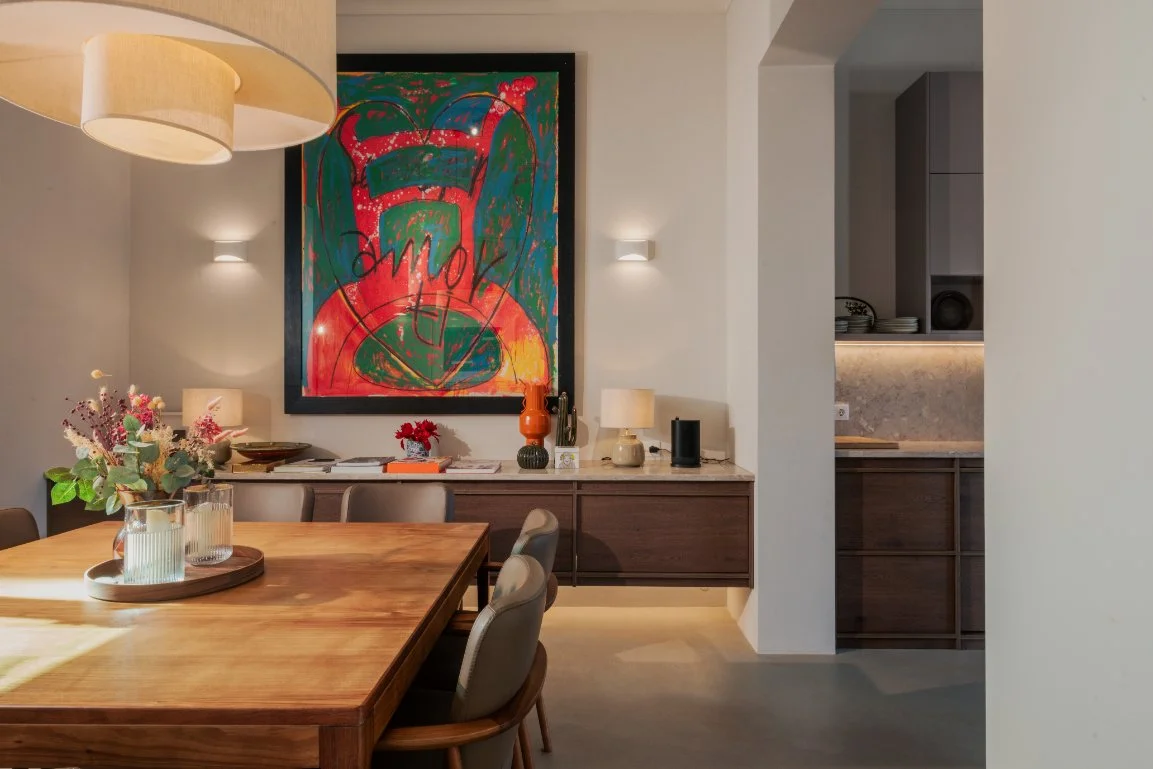 Interior view of a dining room with a wooden table, beige chairs, a sideboard with decorative lamps and vases, a colorful abstract painting on the wall.  Holiday rental home in Lagoa.