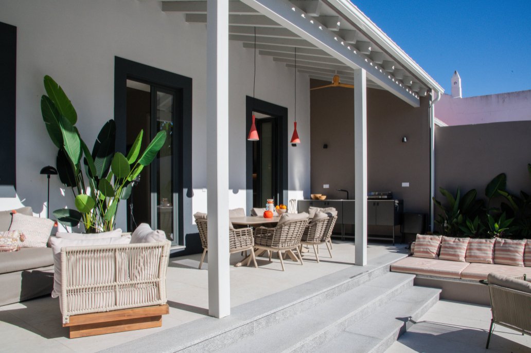 Outdoor patio with dining table, chairs, and outdoor kitchen area, surrounded by greenery and modern house.  Holiday rental home in Lagoa.