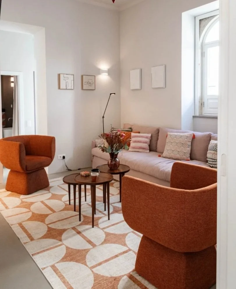 A cozy living room with a white sofa, two rust-colored armchairs, and two small round wooden coffee tables. The sofa has decorative pillows, and a vase with flowers is on one of the tables.  Holiday rental home in Lagoa.