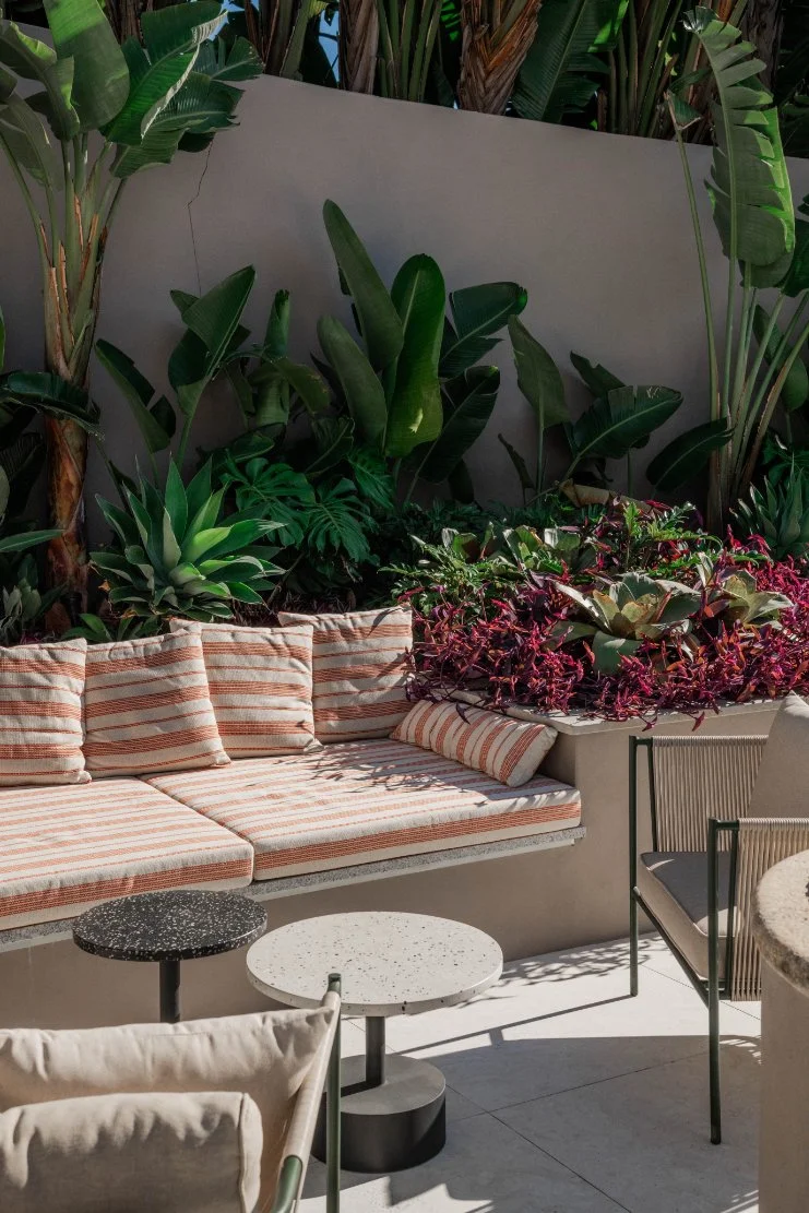 Outdoor seating area with striped cushioned bench, potted plants, and small round tables in sunny weather.  Holiday rental home in Lagoa.