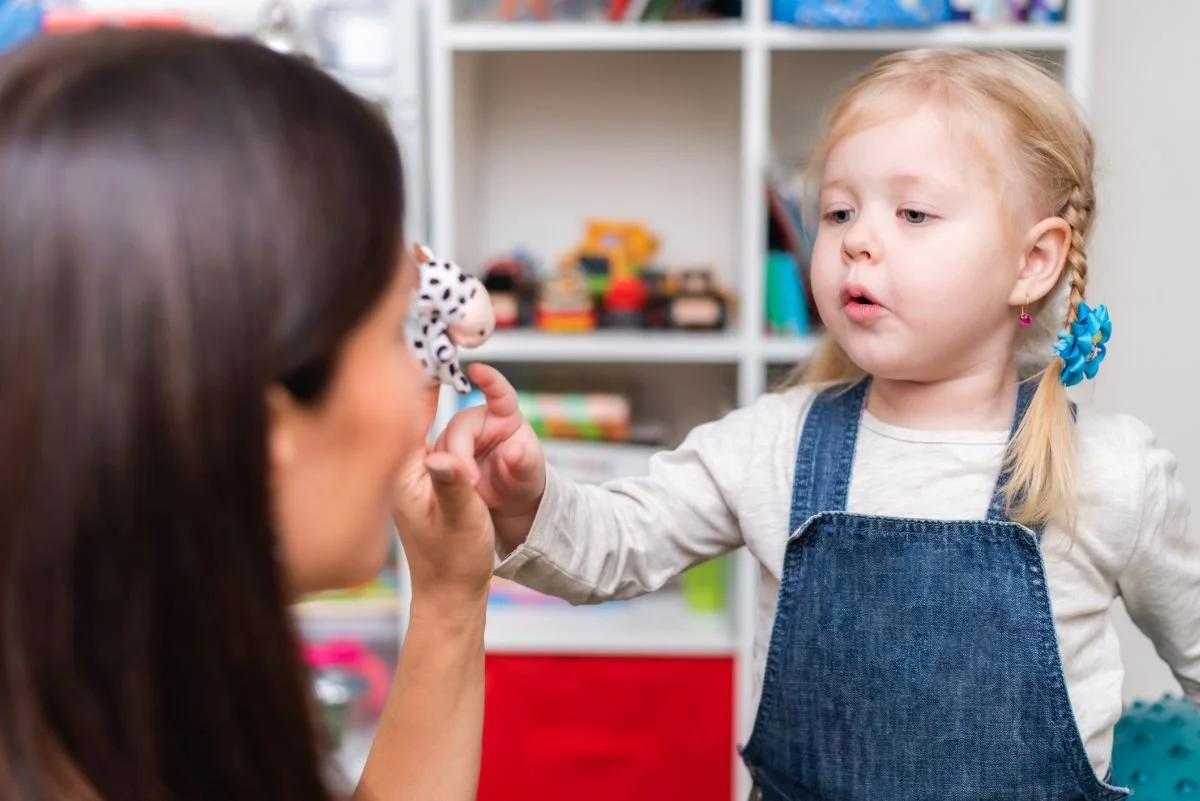 Kleines Mädchen übt mit Logopädin und Spielfigur das Sprechen – Logopädie bei Sprachentwicklungsverzögerung