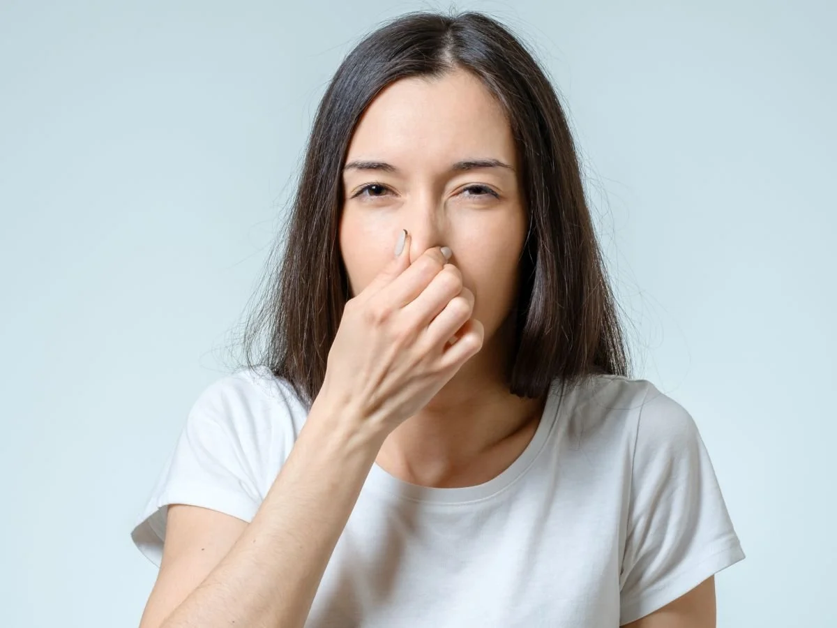 Frau hält sich die Nase zu vor hellblauem Hintergrund – Symbolbild für Rhinophonie und näselnde Aussprache