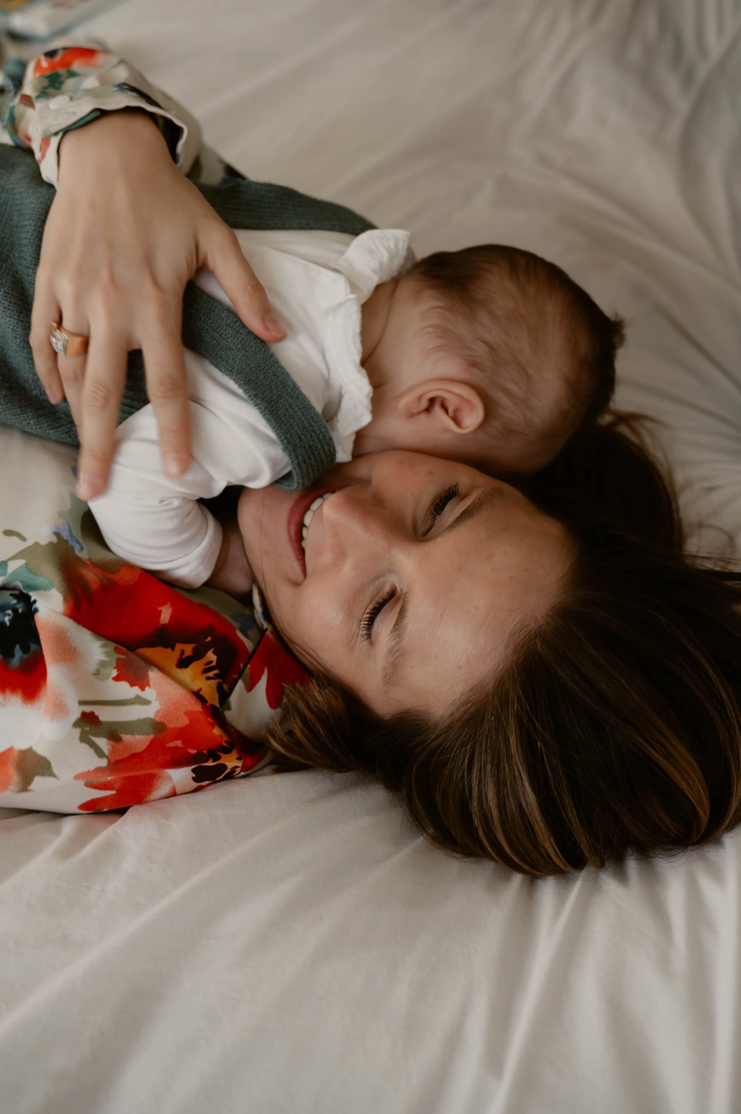 Une femme allongée sur un lit tenant un bébé dans ses bras, tous deux souriants et semblant heureux.