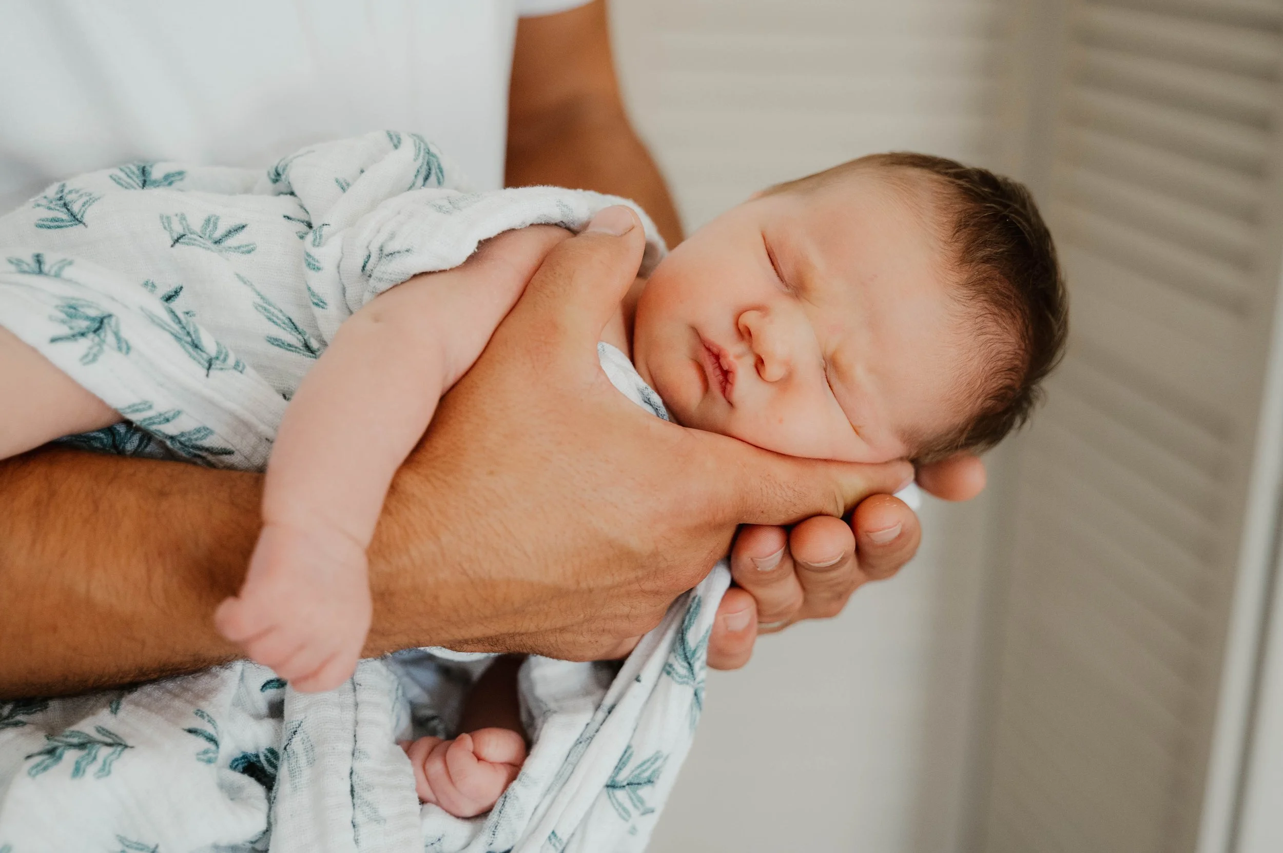 Un bébé endormi dans les bras d'un adulte, enveloppé dans une couverture avec un motif de feuilles