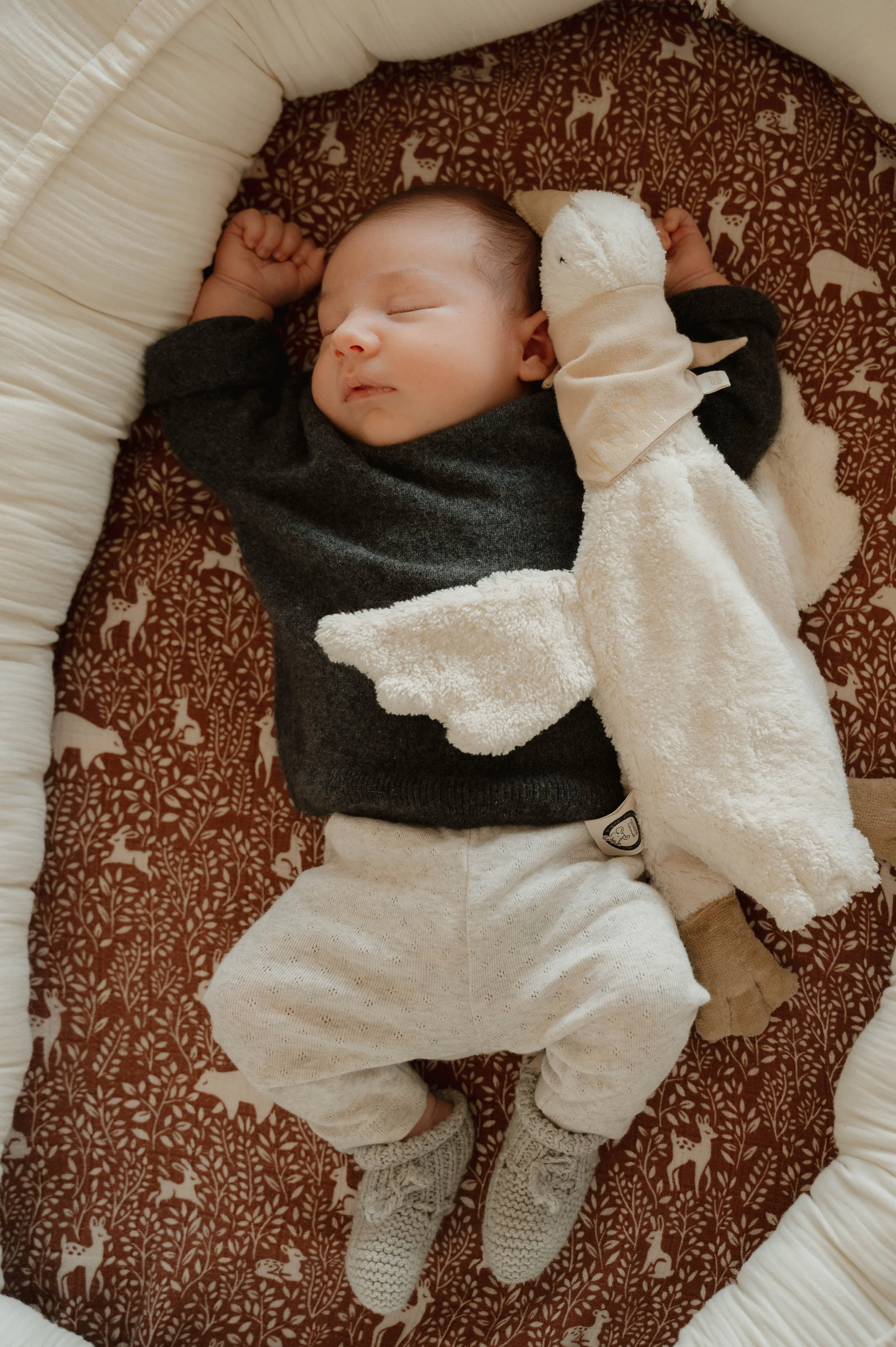 Bébé endormi dans un berceau avec une couverture et un doudou en forme d'oiseau, sur un drap avec motifs d'animaux forestiers.
