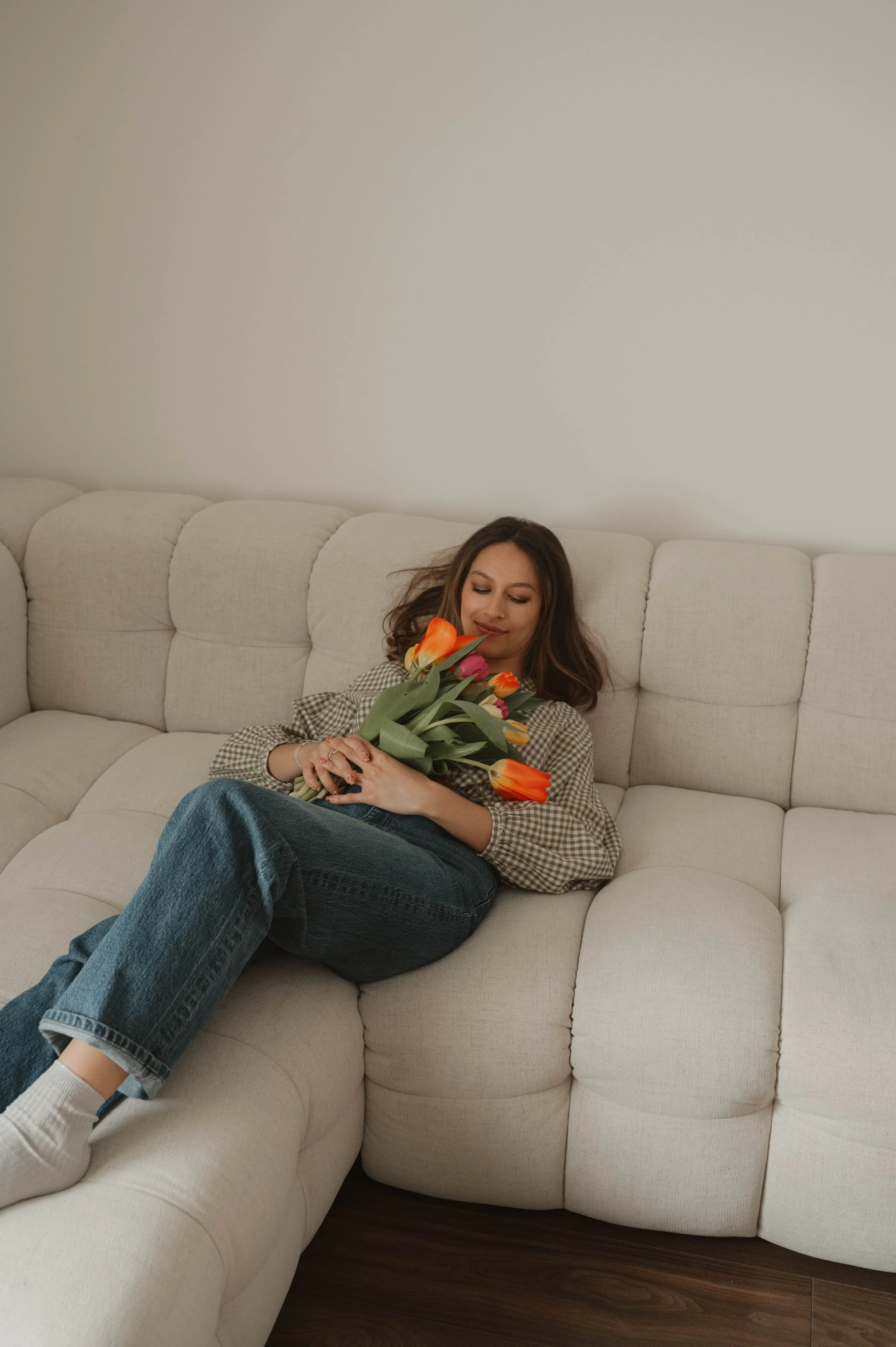 Une personne allongée sur un canapé beige tenant un bouquet de tulipes orange.
