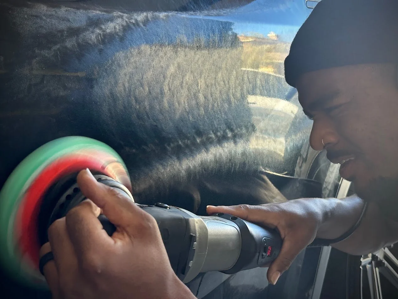 A person car polishing with a electric polisher, wearing a dark head covering, focusing on the car's surface.