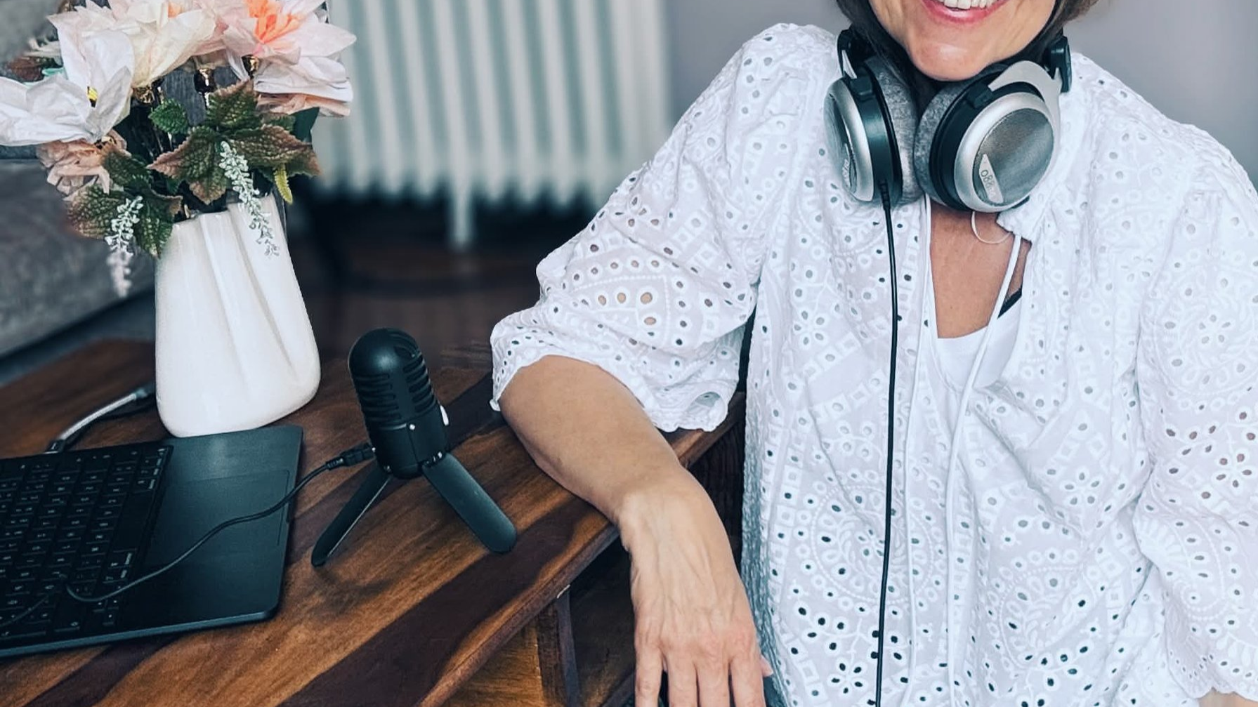 Business-Podcast Experte Kathrin Pabst mit Headset sitzt am Tisch, neben Laptop, Mikrofon und Vase mit Blumen.