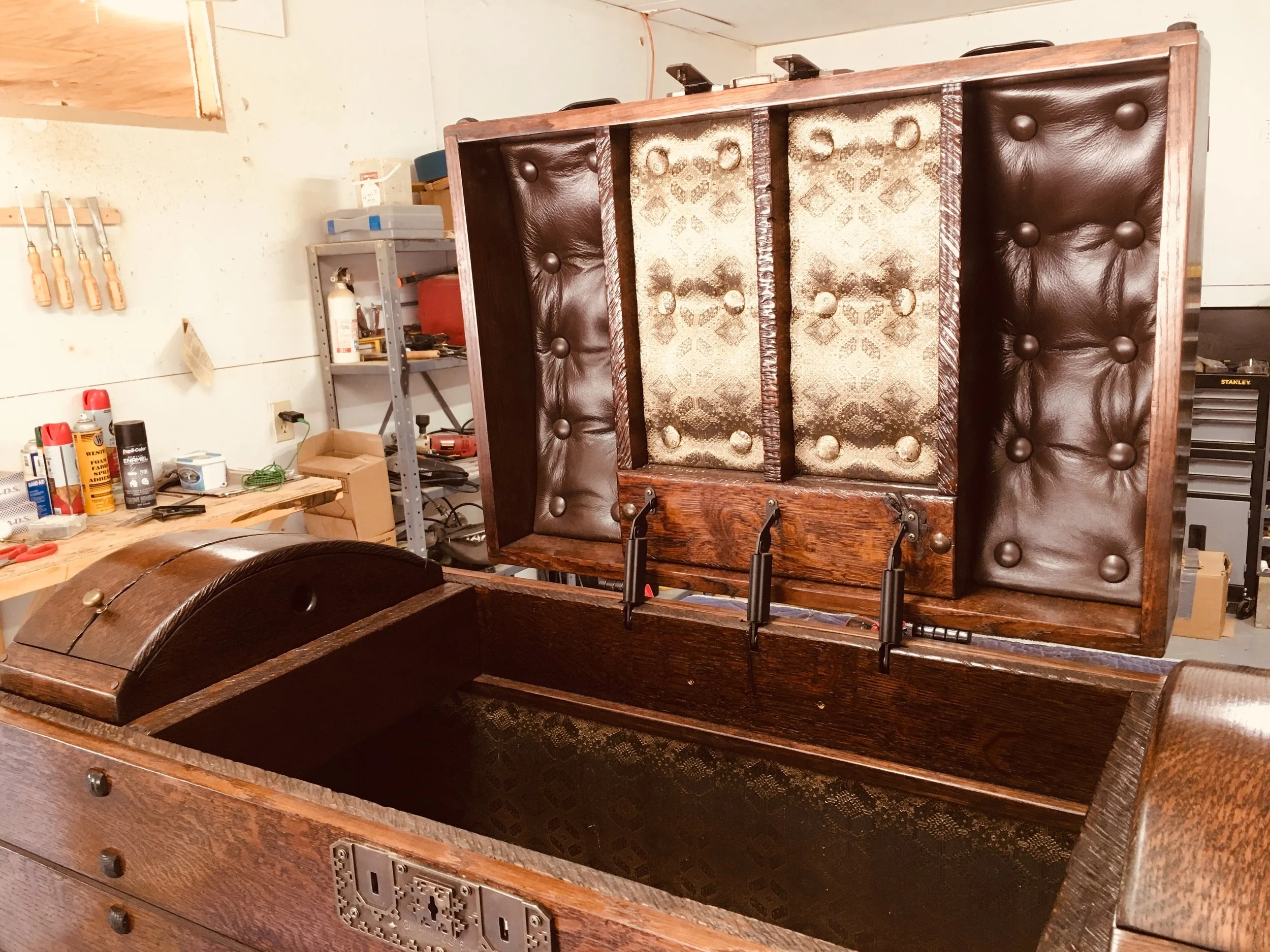 Open antique wooden chest with padded leather interior in a workshop setting, tools and supplies in the background.