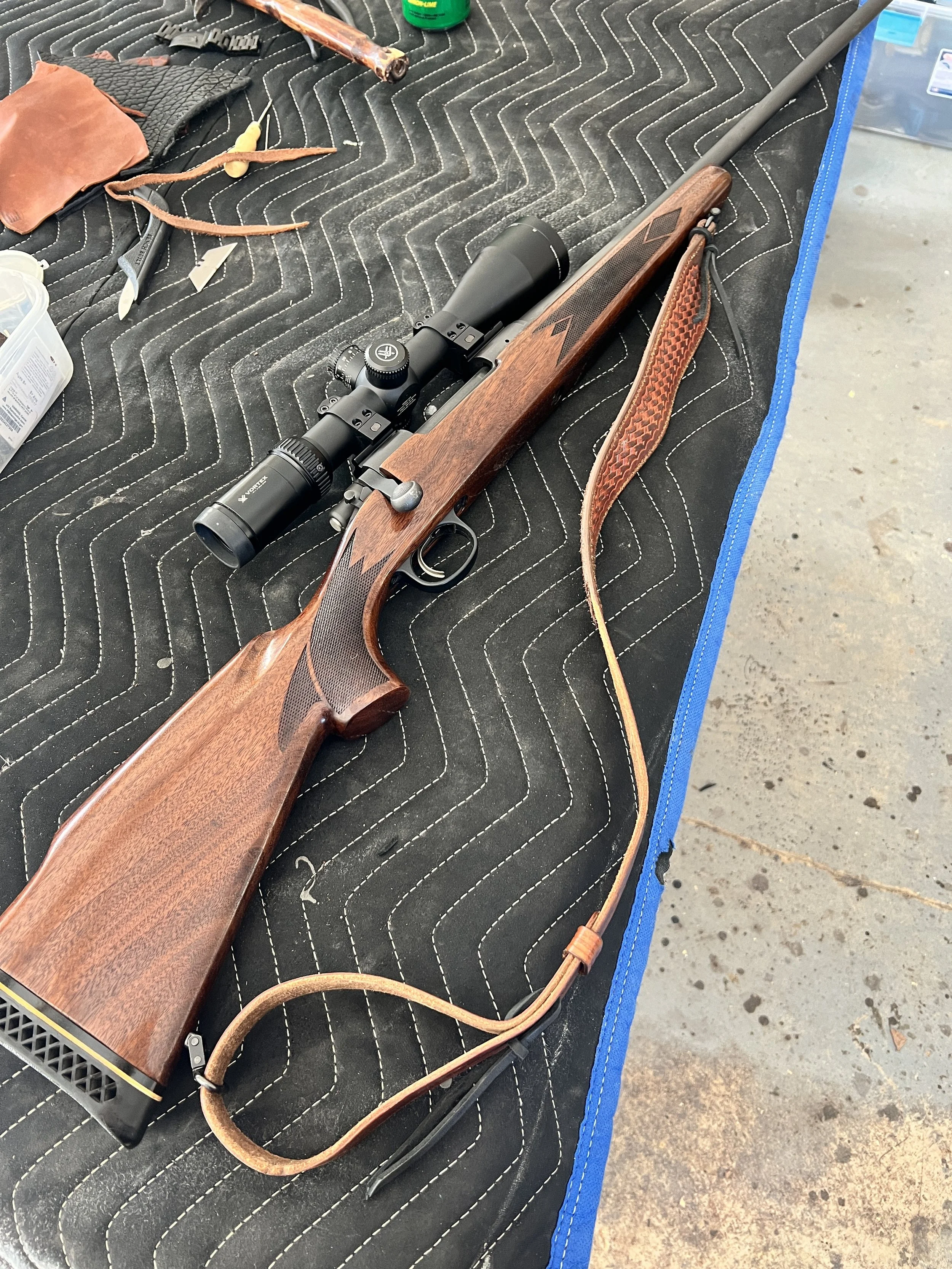 A hunting rifle with a scope placed on a padded surface, surrounded by tools and materials.