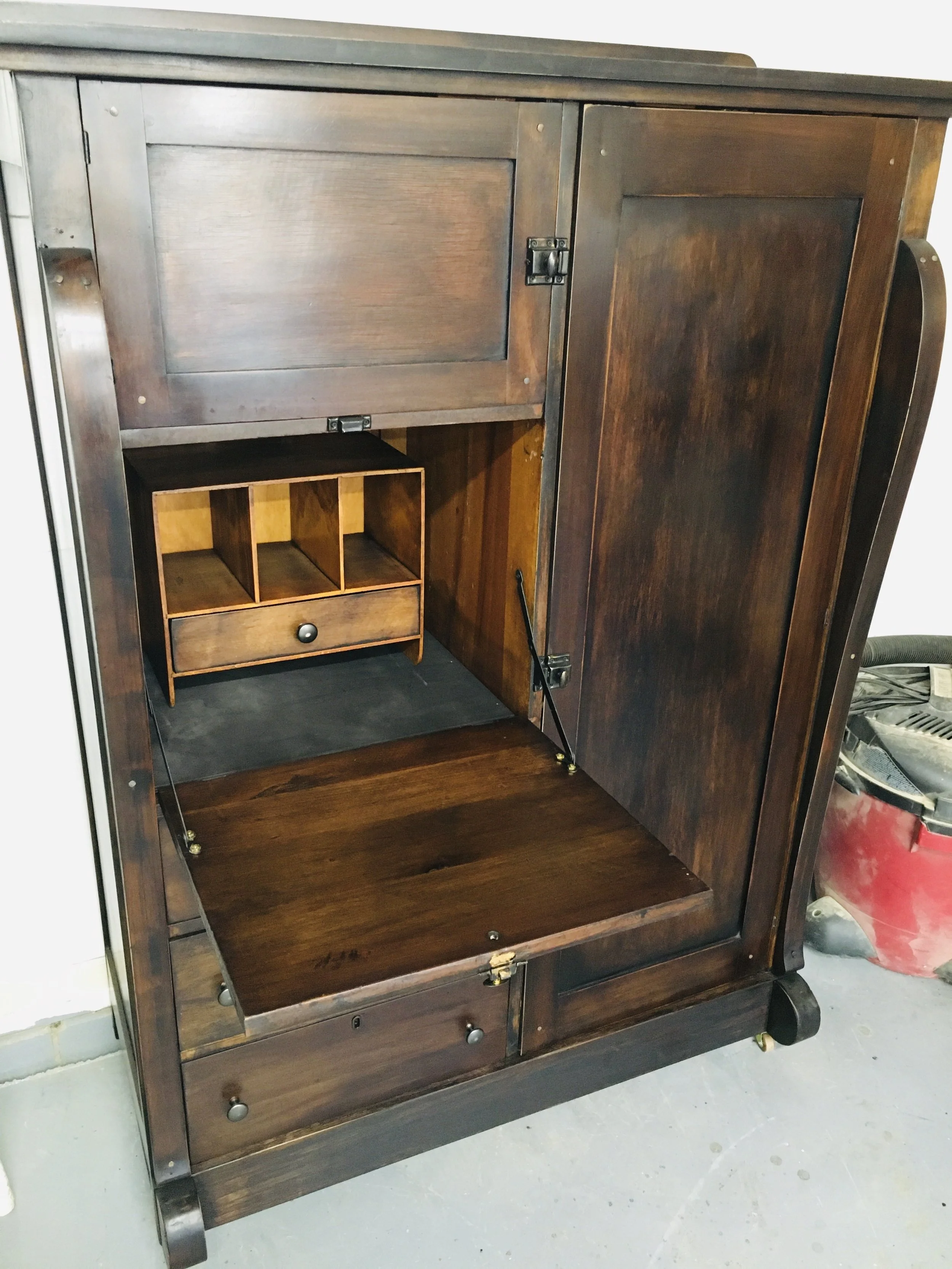 An open vintage wooden secretary desk with compartments and drawers, featuring an extended writing surface at the bottom.