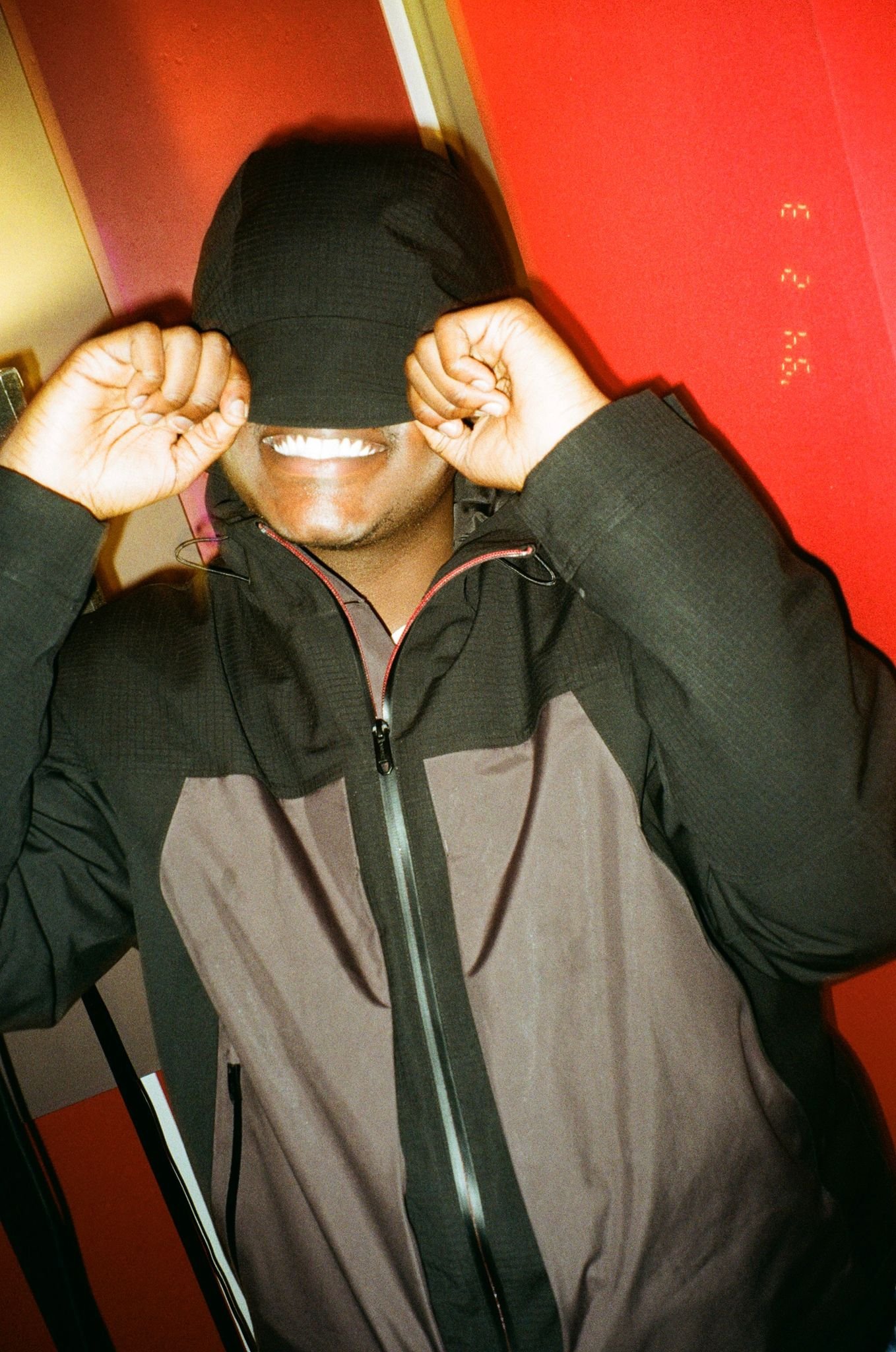 Person in black jacket pulling hood over face with red background