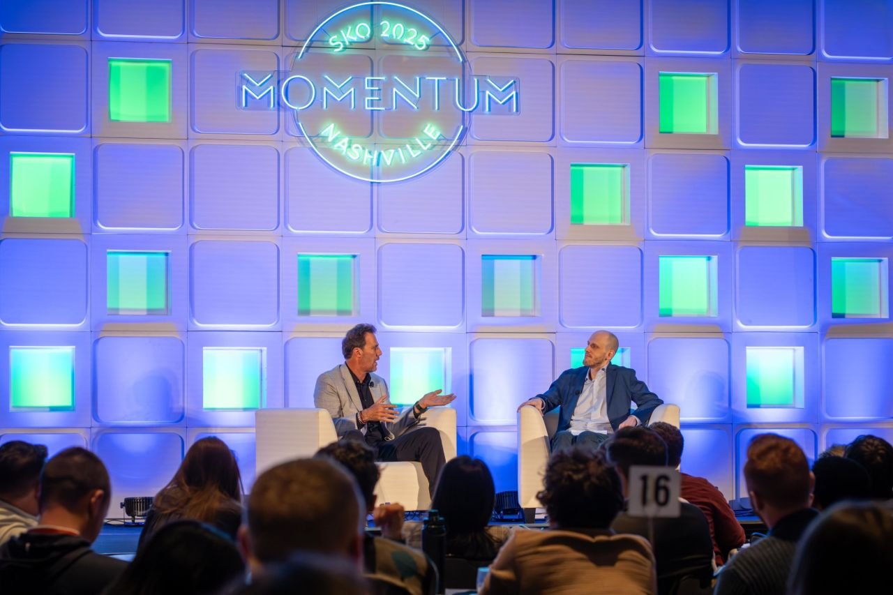Two speakers sitting on stage at Momentum 2025 event in Nashville, addressing an audience.
