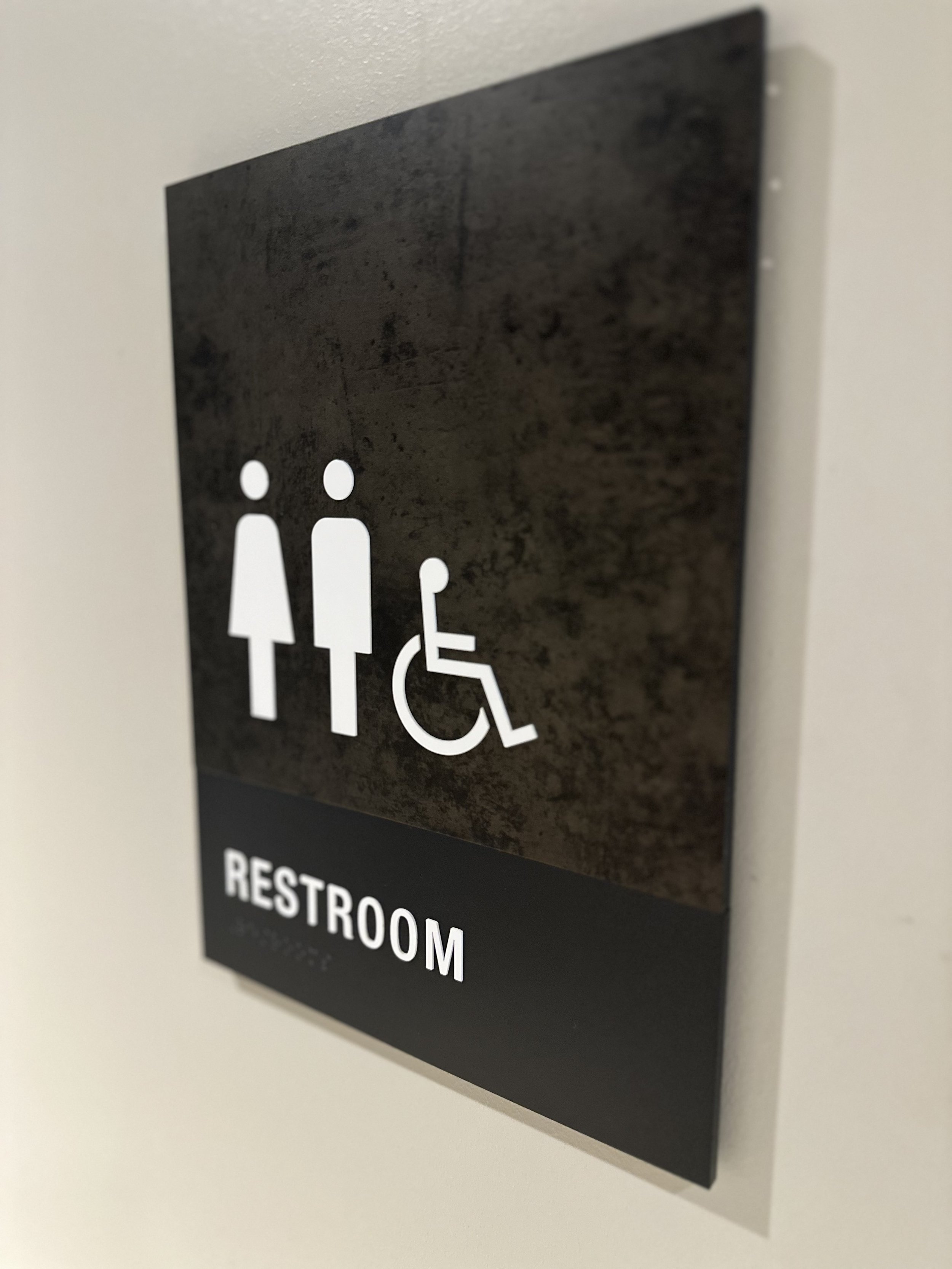 Restroom sign with male, female, and wheelchair accessible symbols, Braille included.