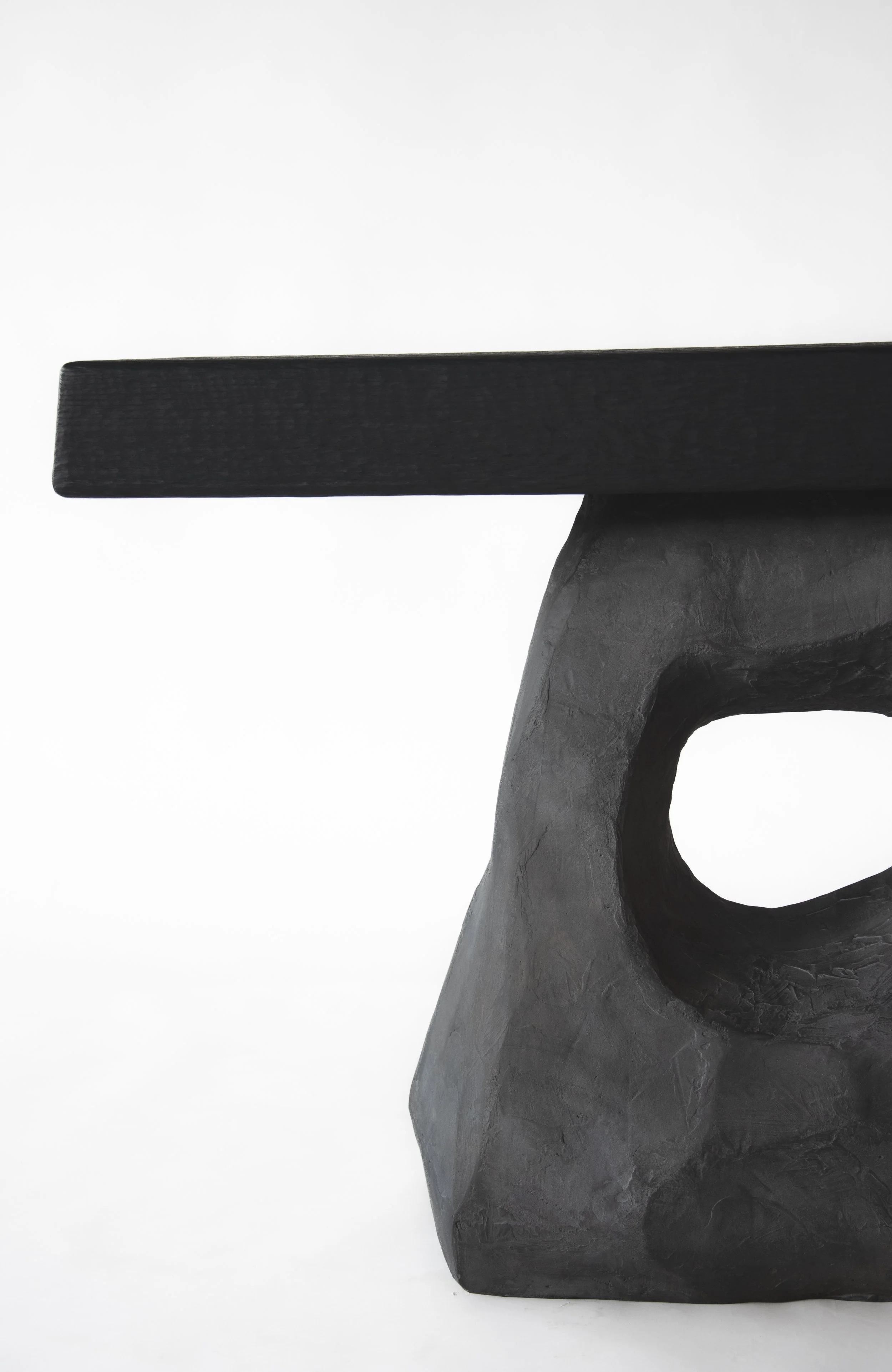 Close-up of a modern black wooden table with a sculptural stone base against a plain white background.