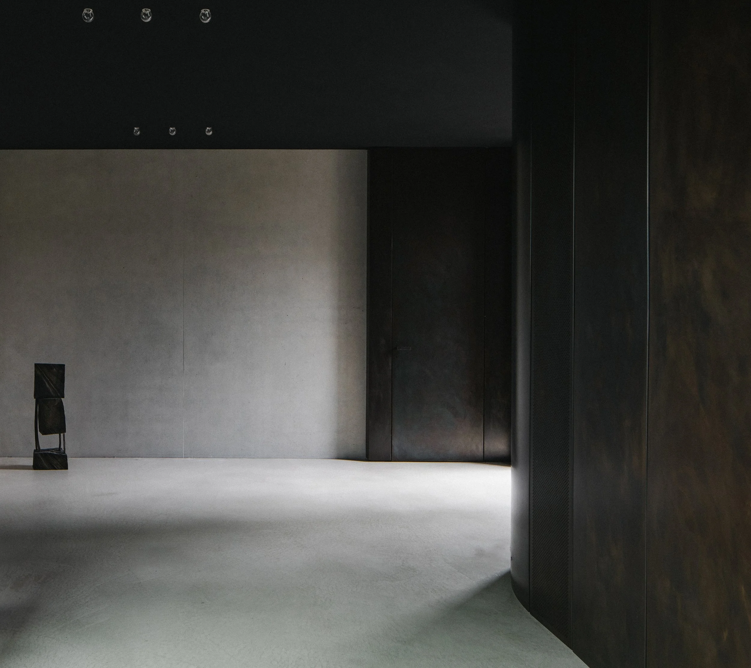 Minimalist interior space with dark walls, a white carpeted floor, and a solitary black sculpture on the floor.