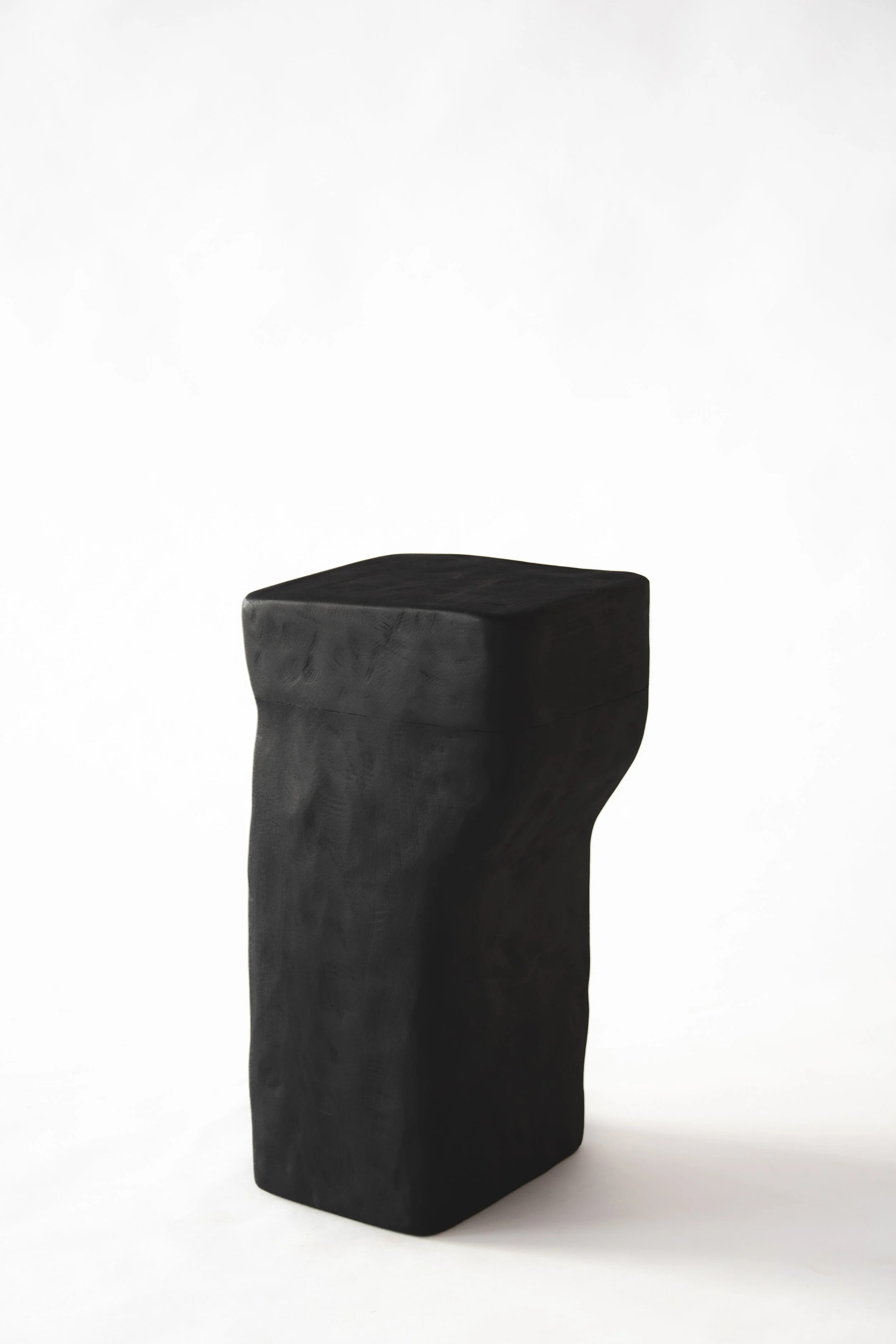 A black, abstract sculpture resembling a human leg and foot, set against a plain white background.