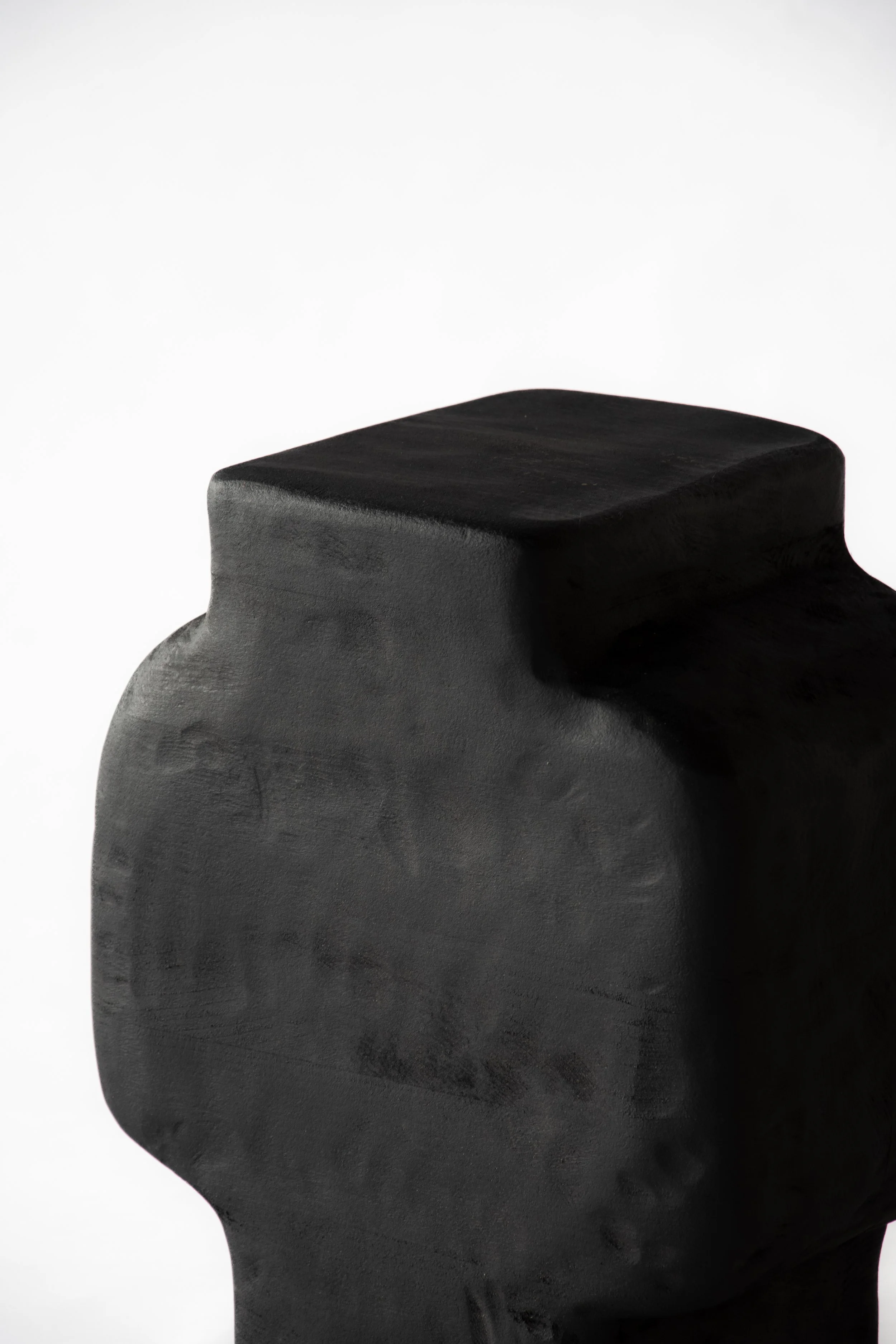A close-up of a black sculpture of a human head with a square shape on top, against a plain white background.