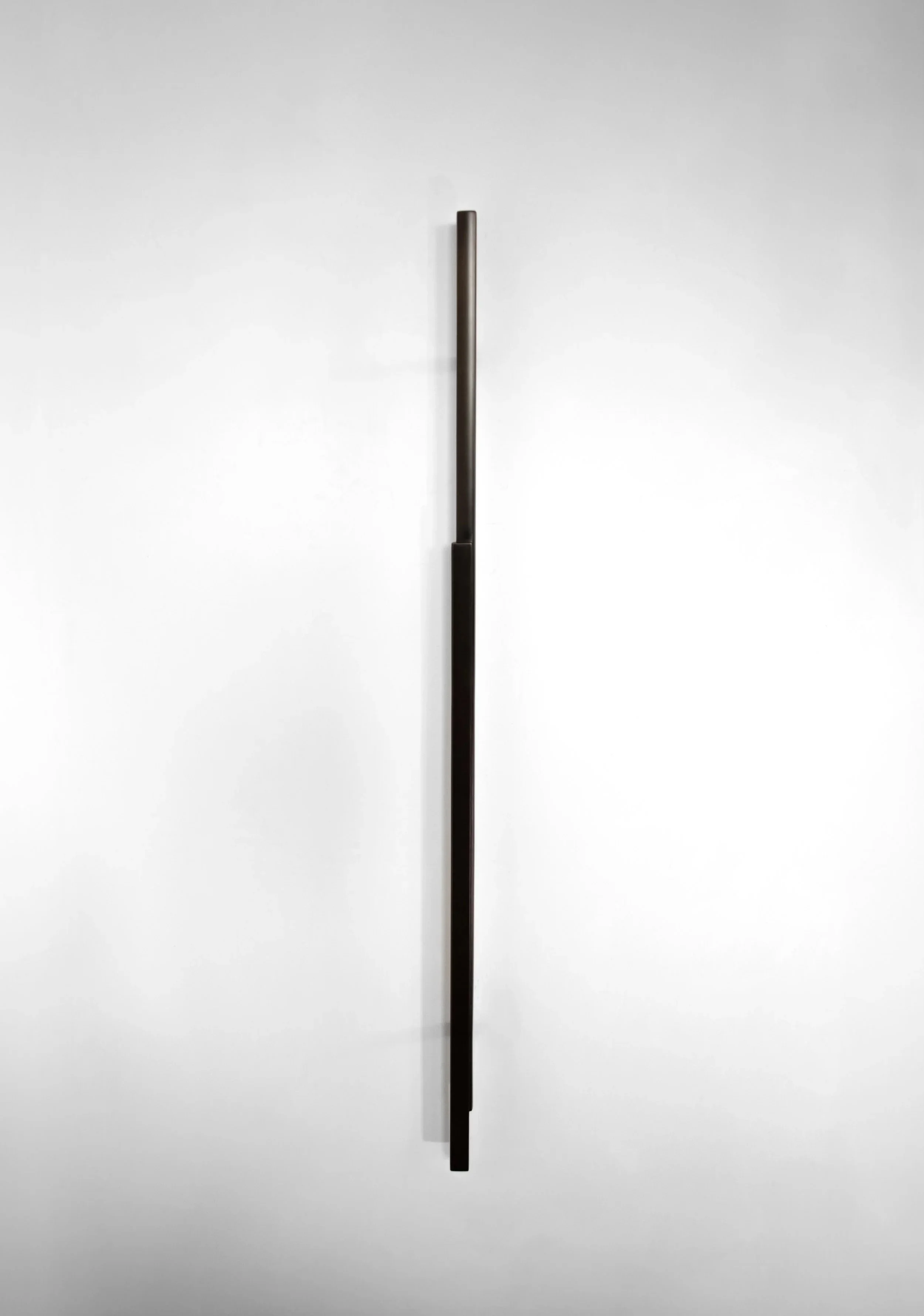 A tall, black, minimalist sculpture mounted on a plain white wall.