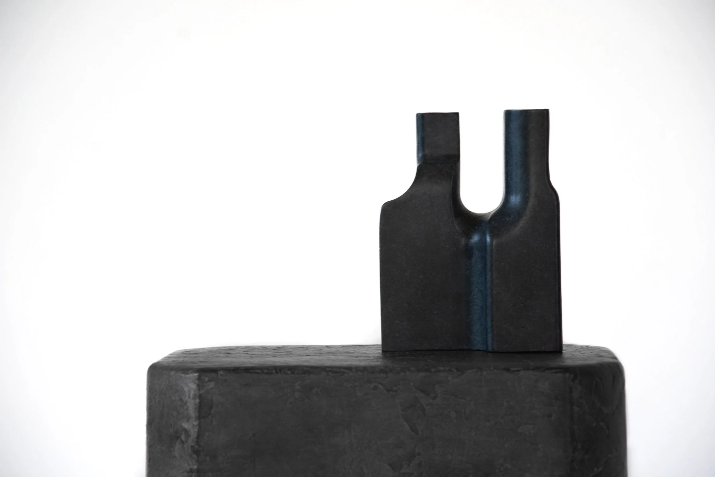 Black art sculpture with a U-shaped cutout, placed on a black platform against a plain white background.