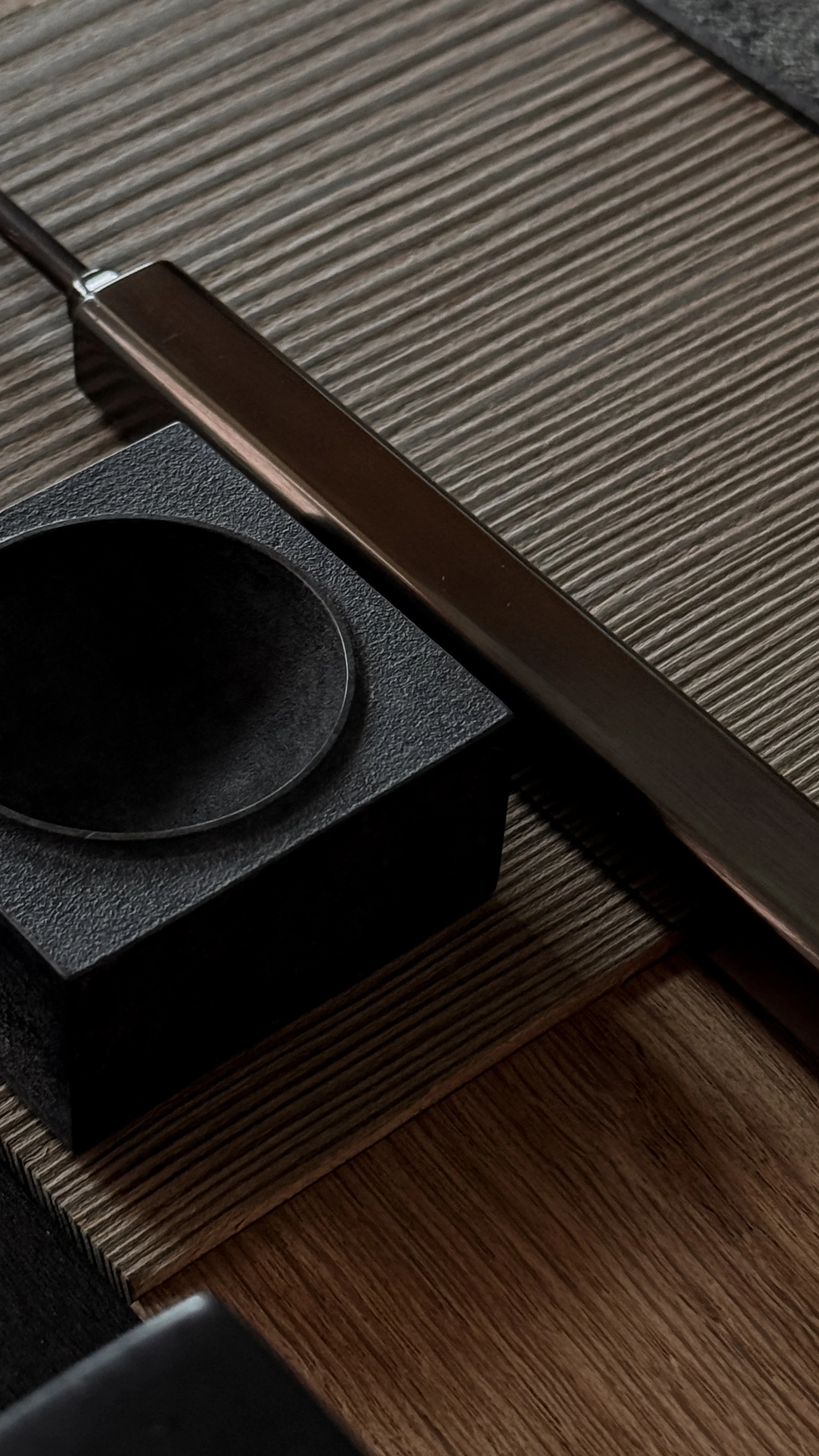 Close-up of a lamp with a flexible neck, placed on a wooden table, with textured black and brown surfaces in the background.
