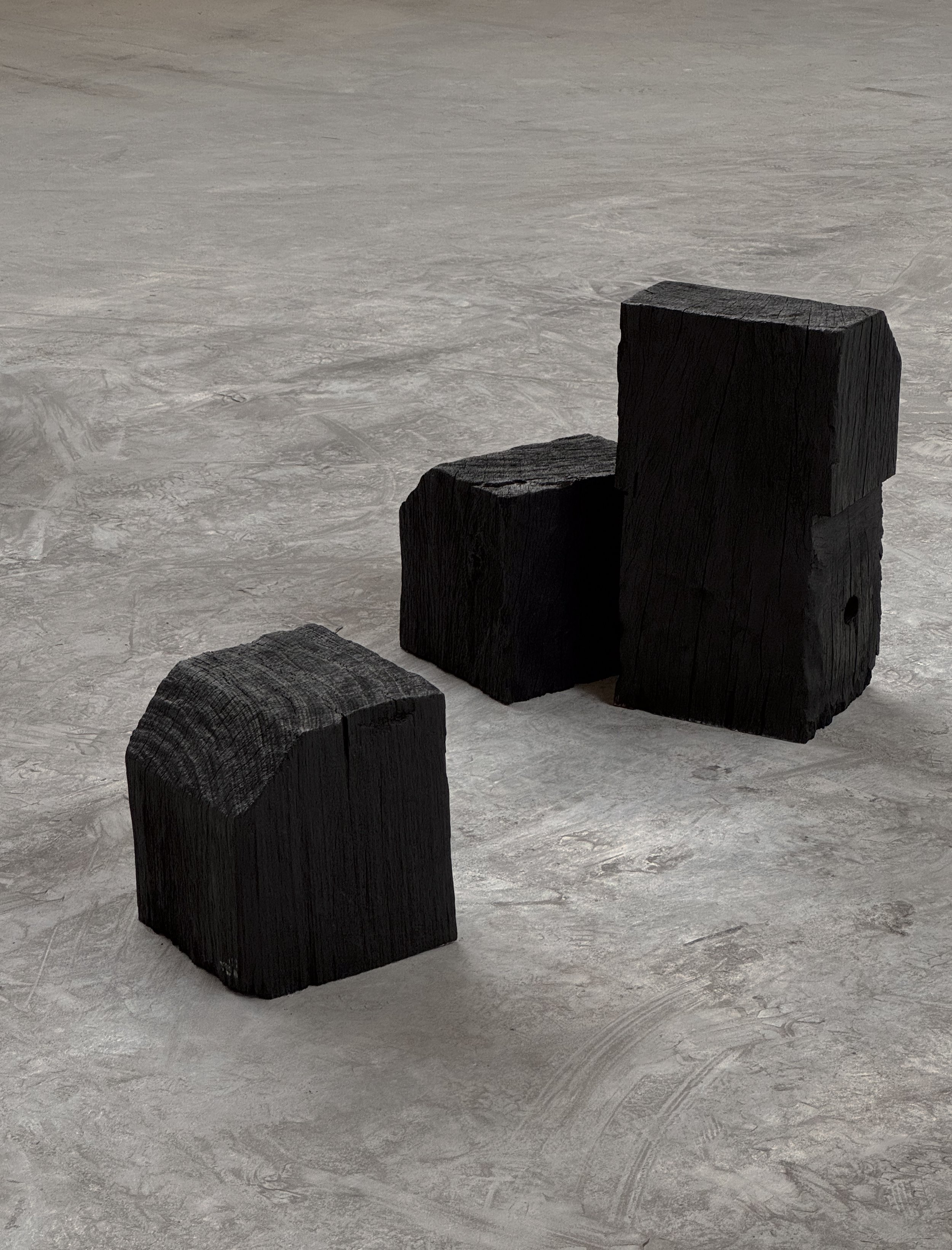 Three black wooden blocks with different shapes placed on a gray textured floor.