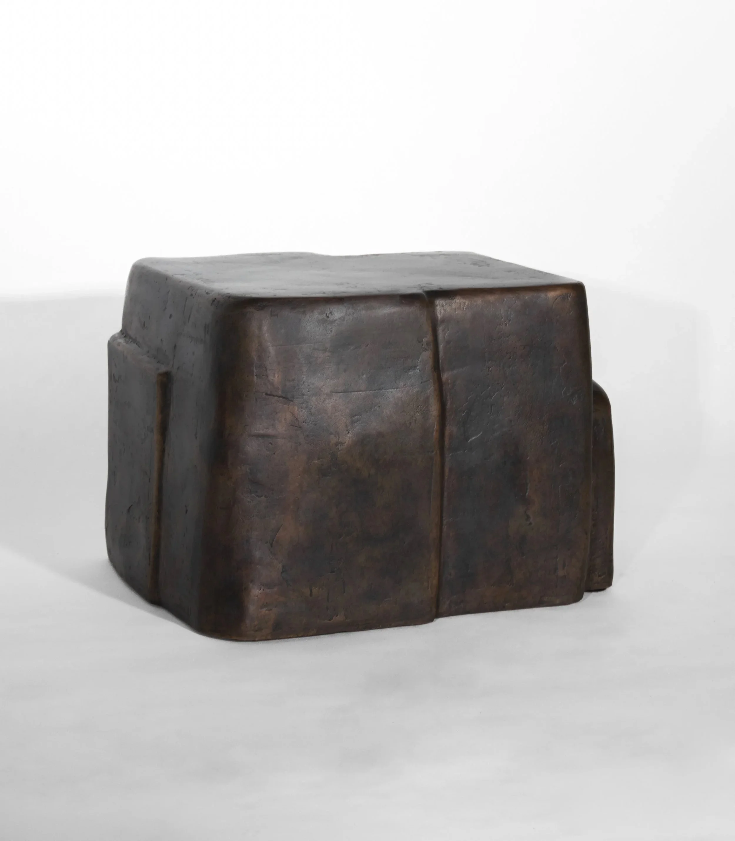 A dark, textured, irregularly shaped stone sculpture against a white background.