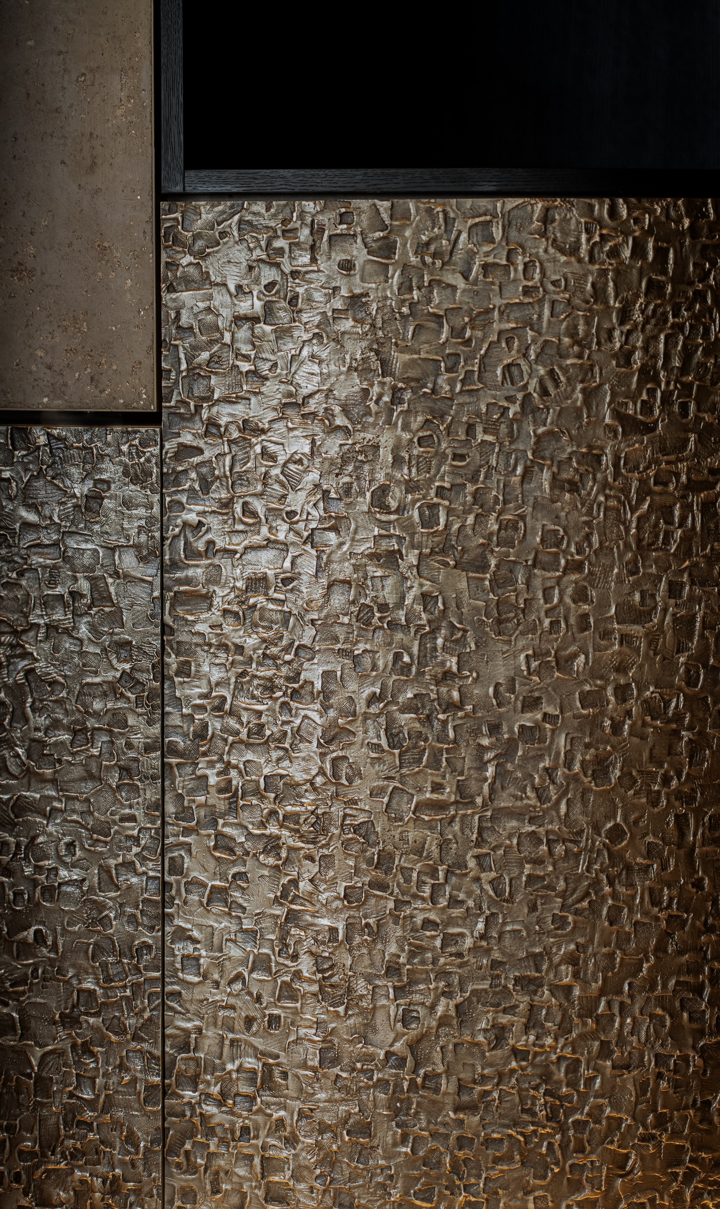 Close-up of a textured, metallic surface with a raised, irregular pattern and a dark background.