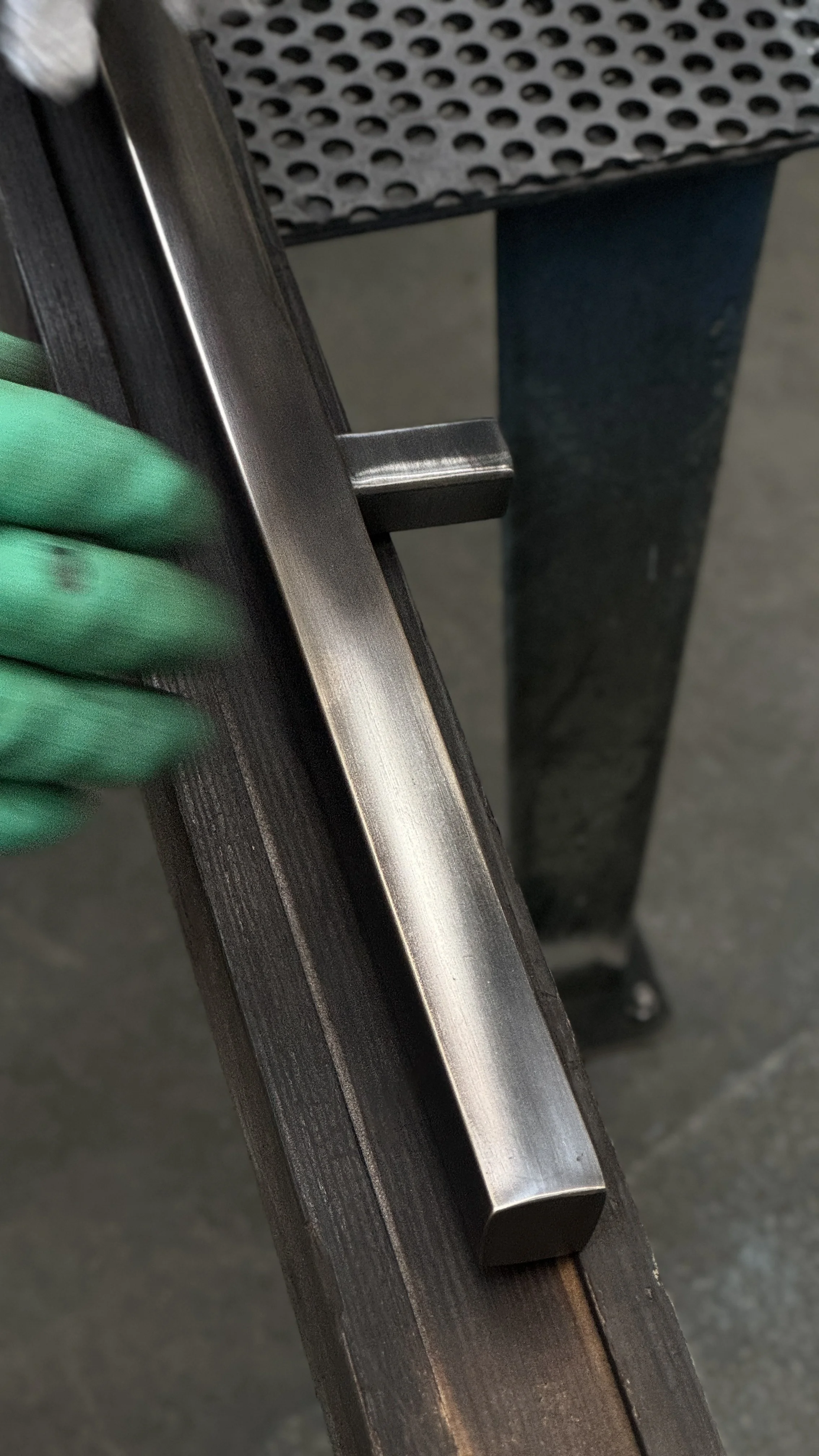 Close-up of a metallic object, possibly a part of industrial equipment, being handled by a person wearing green gloves.