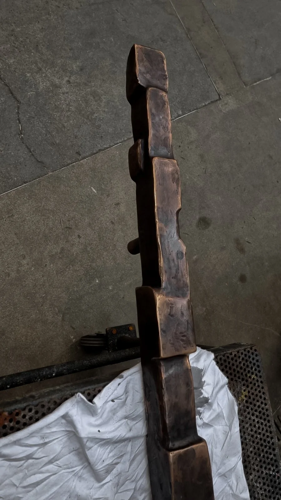 A bronze  object with a textured surface, standing upright on a textured surface with a white cloth draped below it.