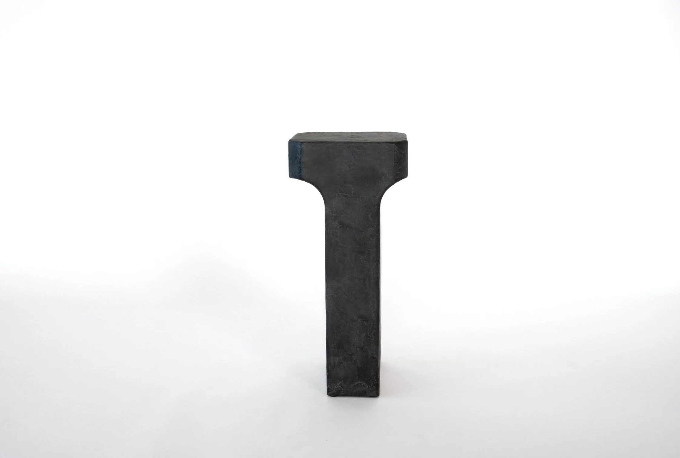 A single black stone or concrete block shaped like the letter 'T' standing upright on a white background.