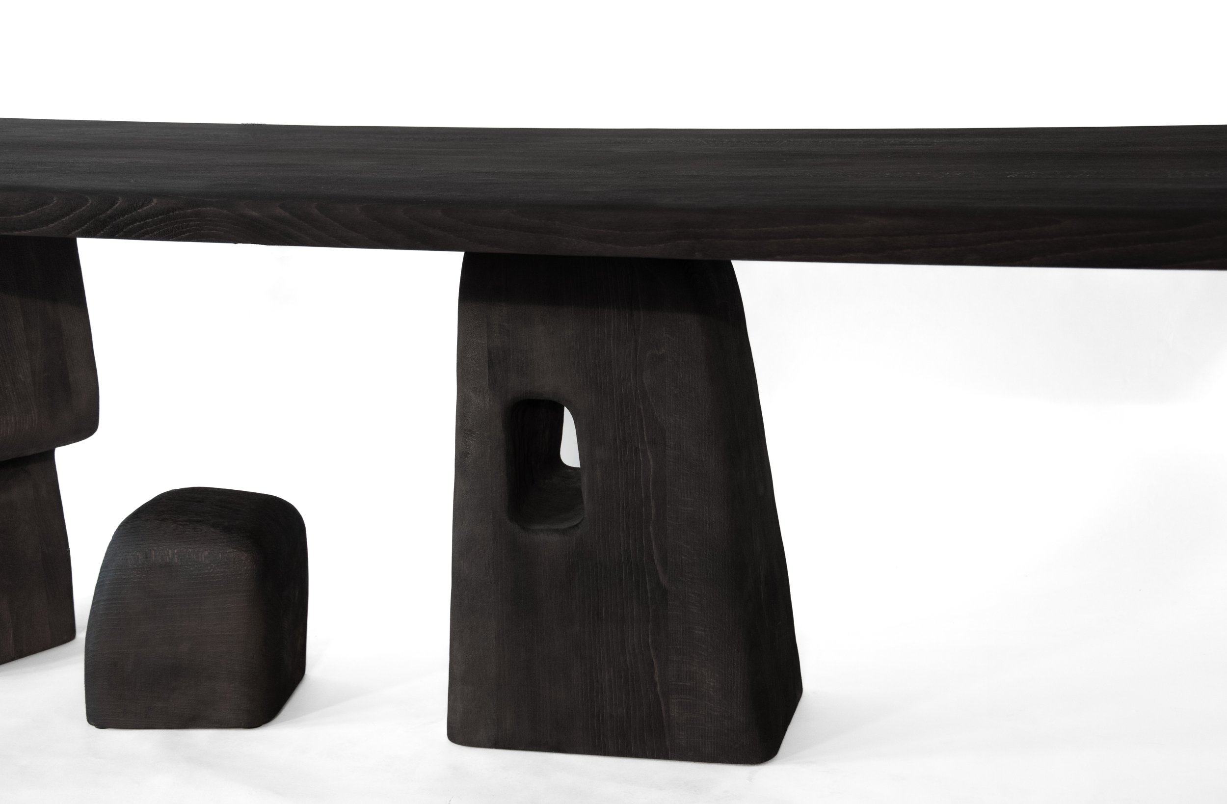 Close-up image of a black wooden table with unique, modern, thick legs on a white background.