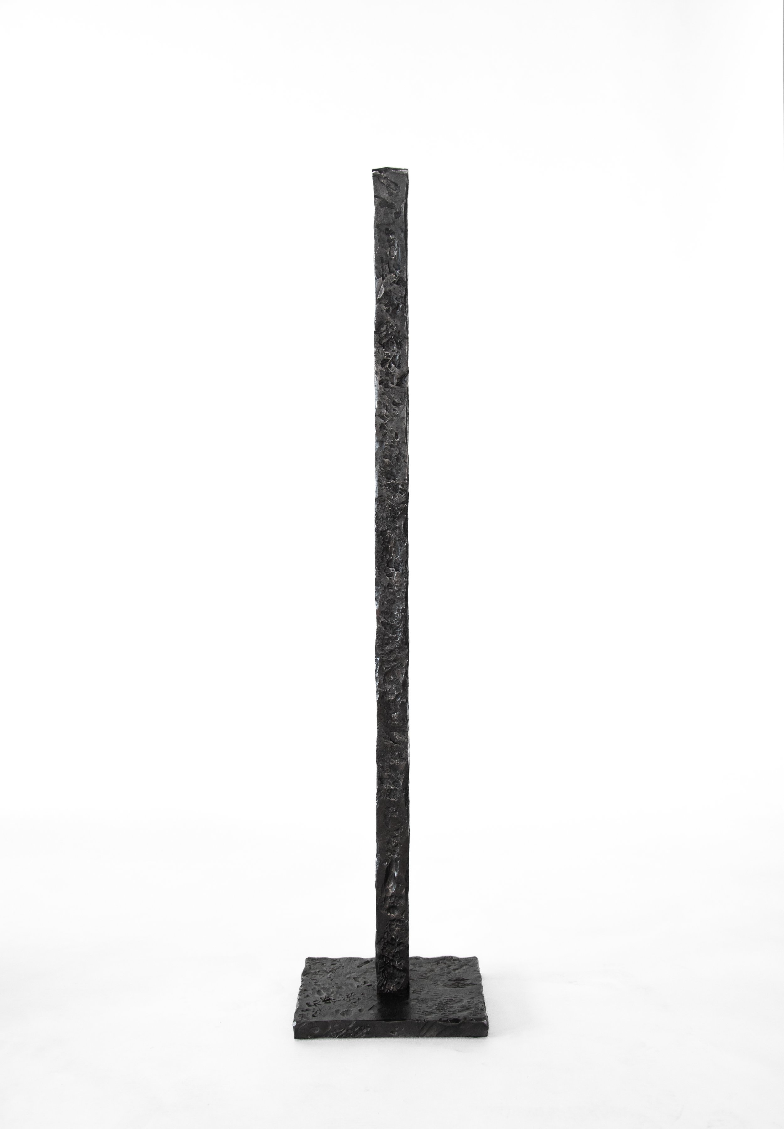 A tall, narrow, black textured sculpture on a square base, standing against a white background.
